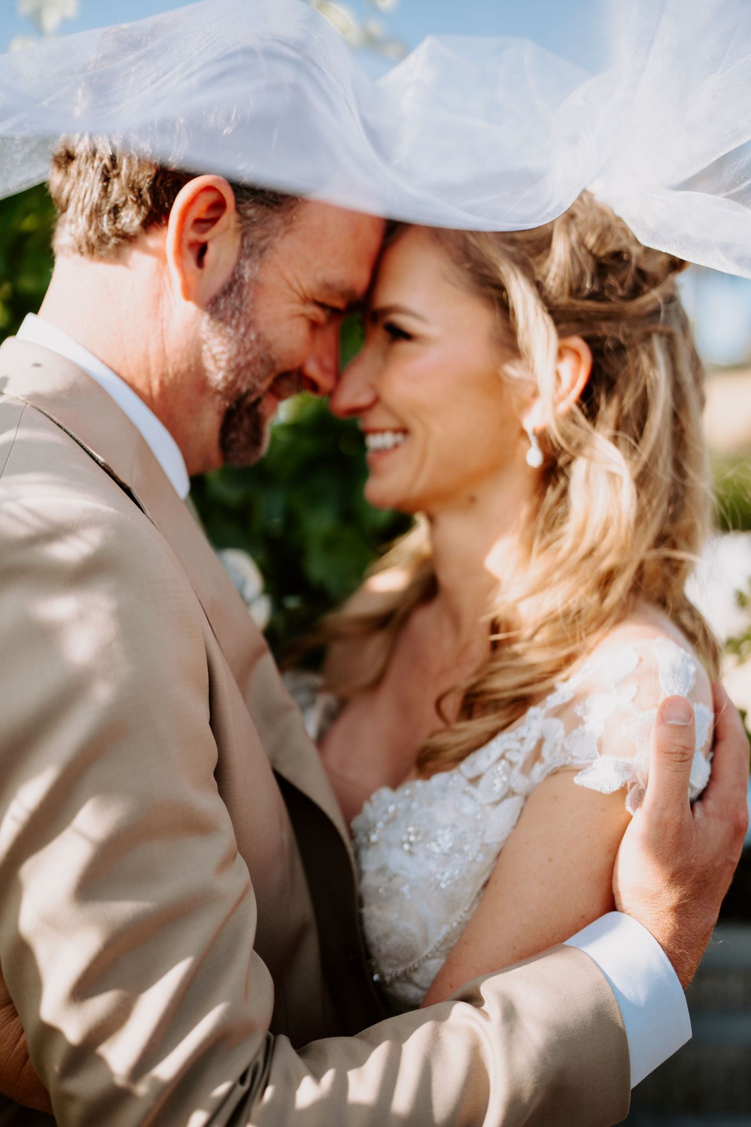 Bride and groom share a romantic forehead touch under a flowing veil on their wedding day.