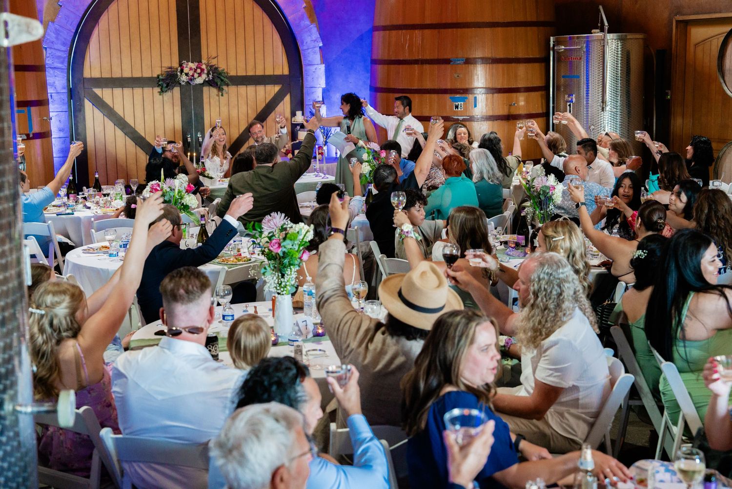 Wedding reception celebration in a rustic barn venue with purple accent lighting.