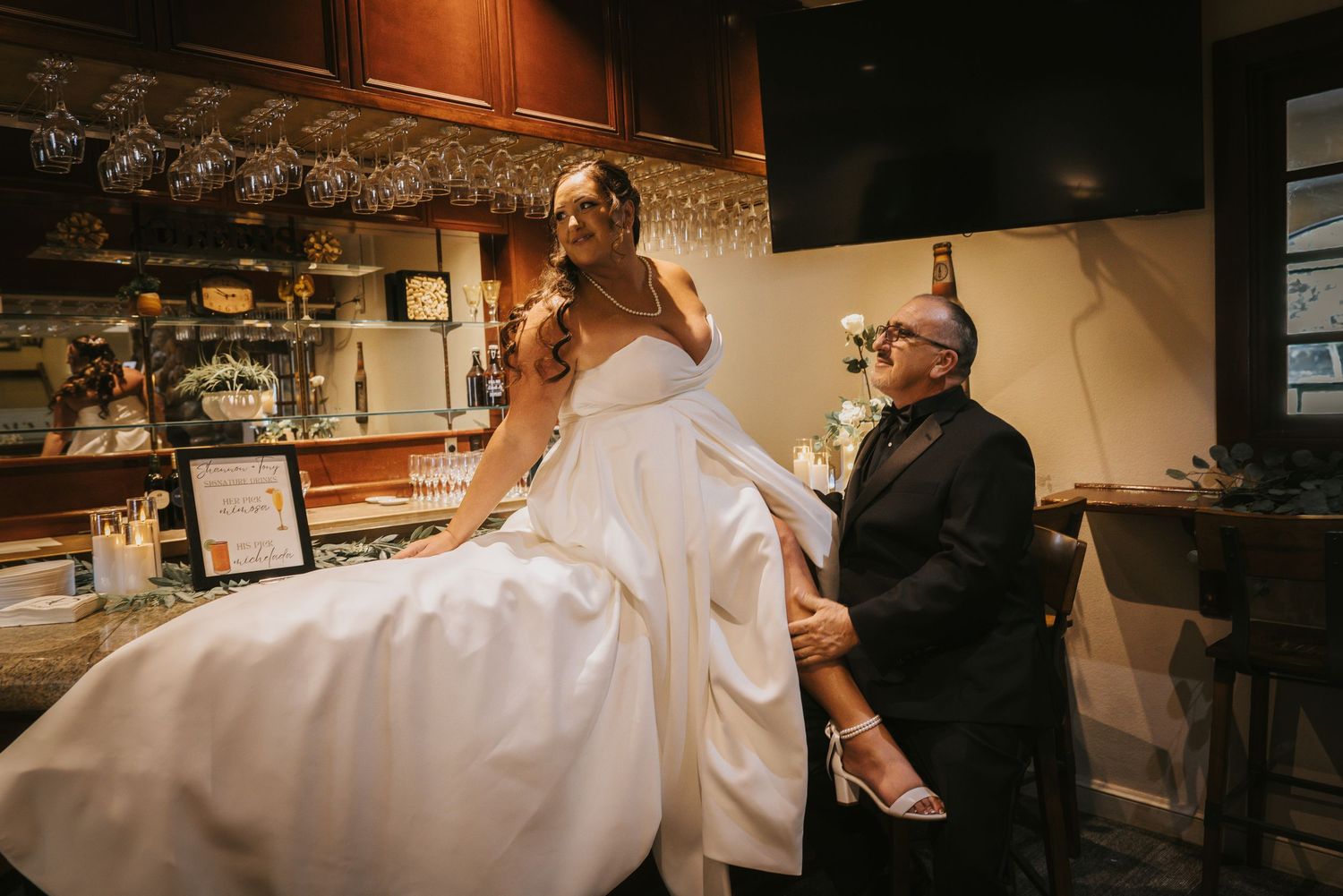 Bride in white wedding gown being helped by a man near a bar, laughing joyfully during wedding preparations at Forest Suits Resorts