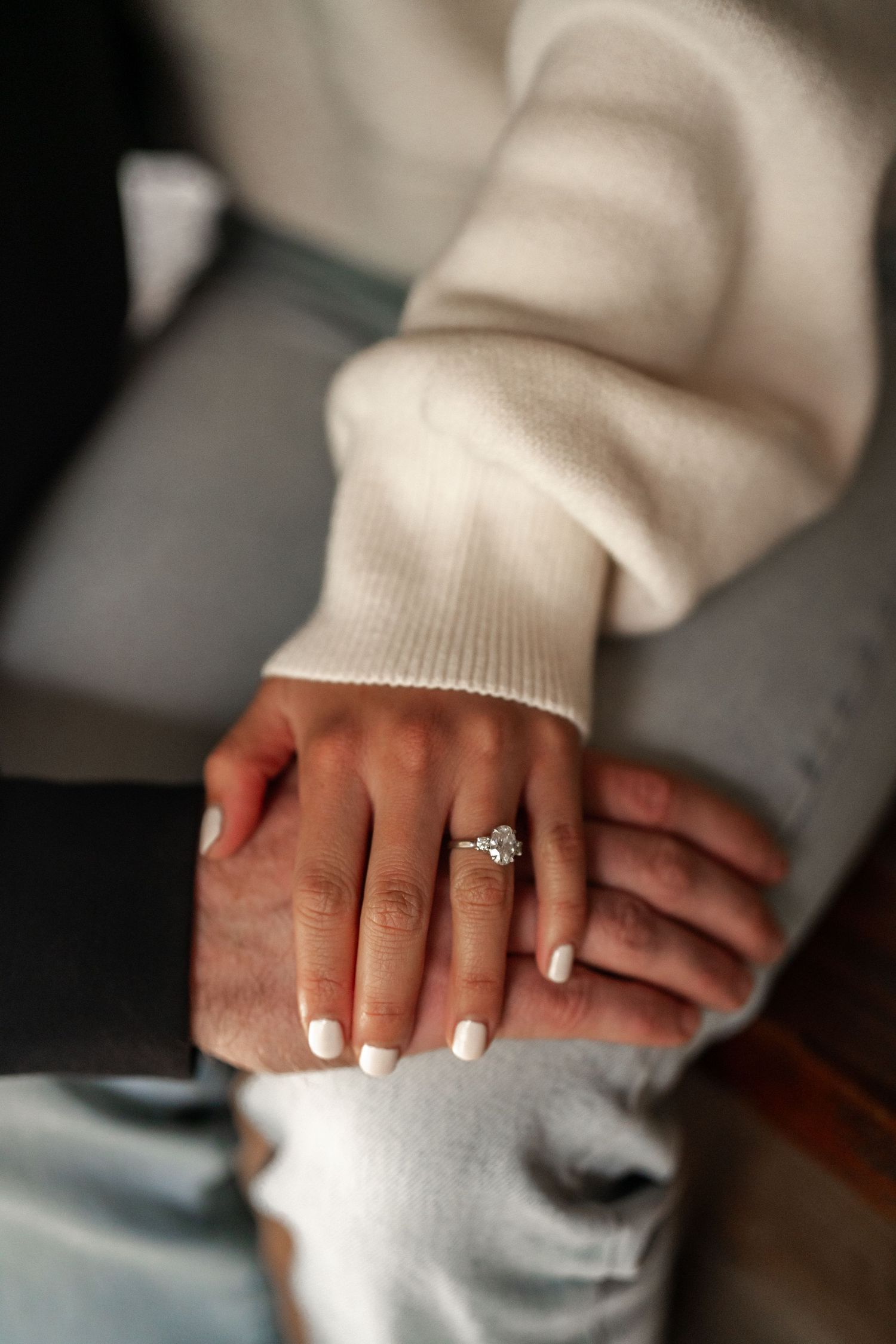 Close-up of engagement ring on hand with white nail polish and cream sweater sleeve.