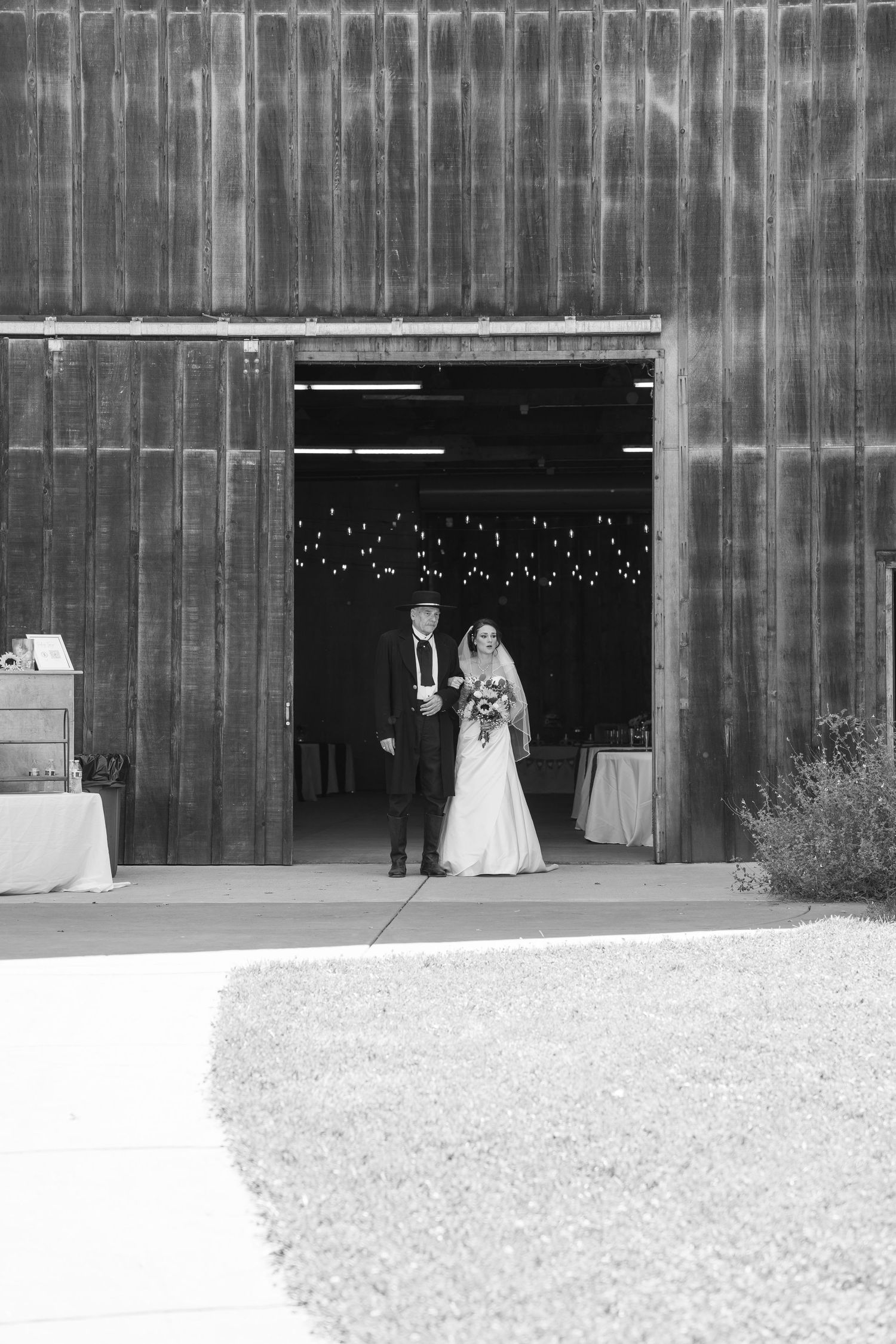 Black and white photo of a bride and groom standing in the doorway of a rustic barn wedding venue.