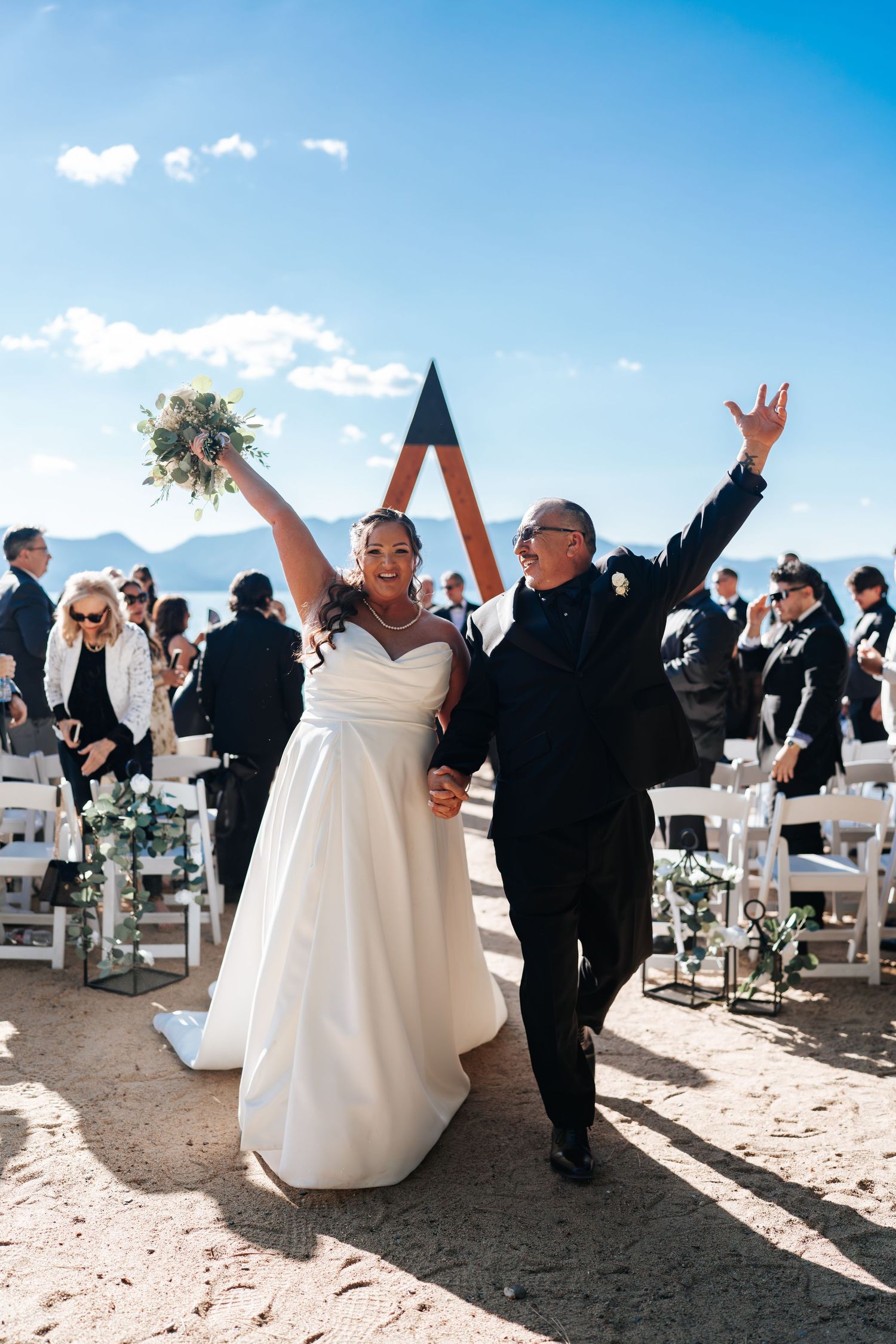 Joyful newlyweds celebrate recessional at outdoor desert wedding ceremony with mountain views and blue sky.