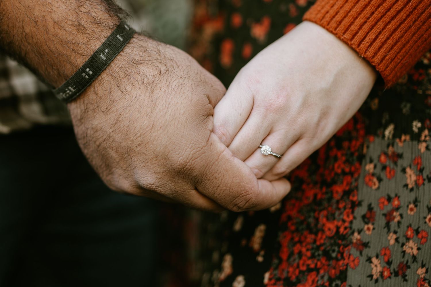 Hands wearing autumn-colored sweaters intertwined against floral pattern.