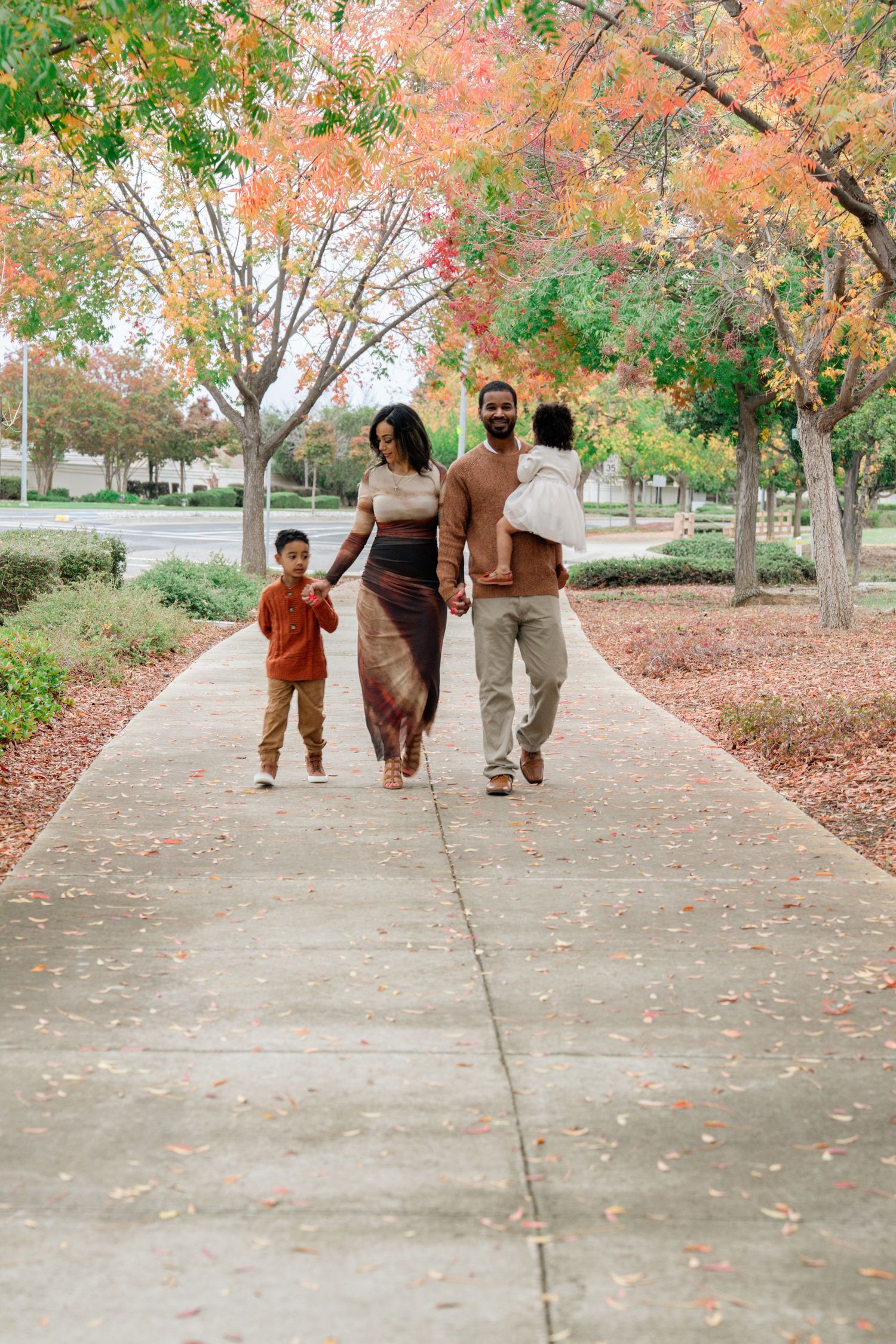 Family walking away on path surrounded by beautiful fall foliage with pink and orange leaves.