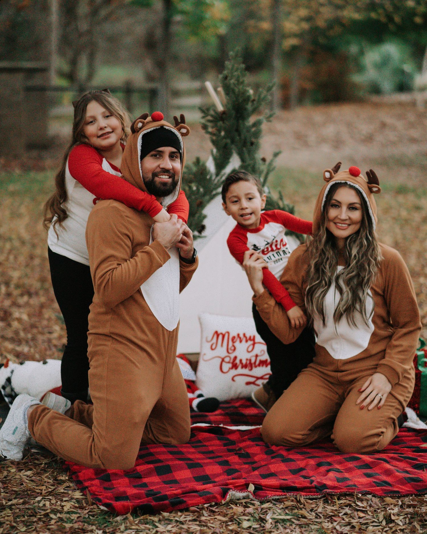 Holiday family photoshoot on red plaid blanket with Christmas decorations outdoors.