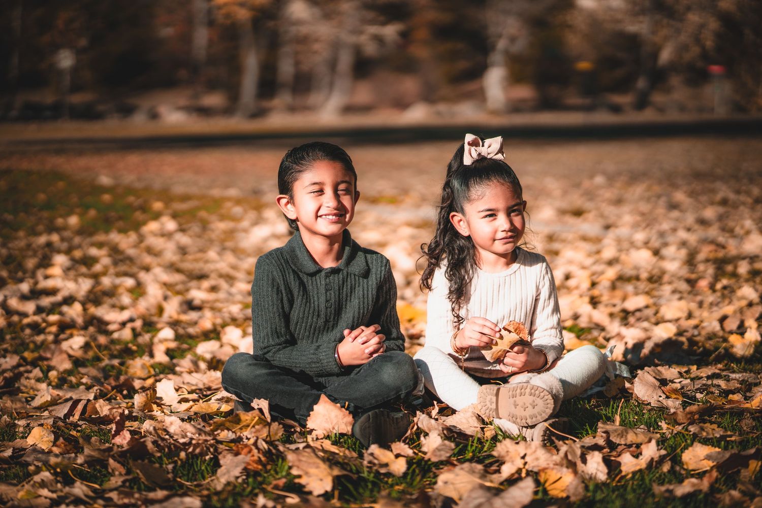 People relaxing on ground covered with fallen autumn leaves in natural lighting.