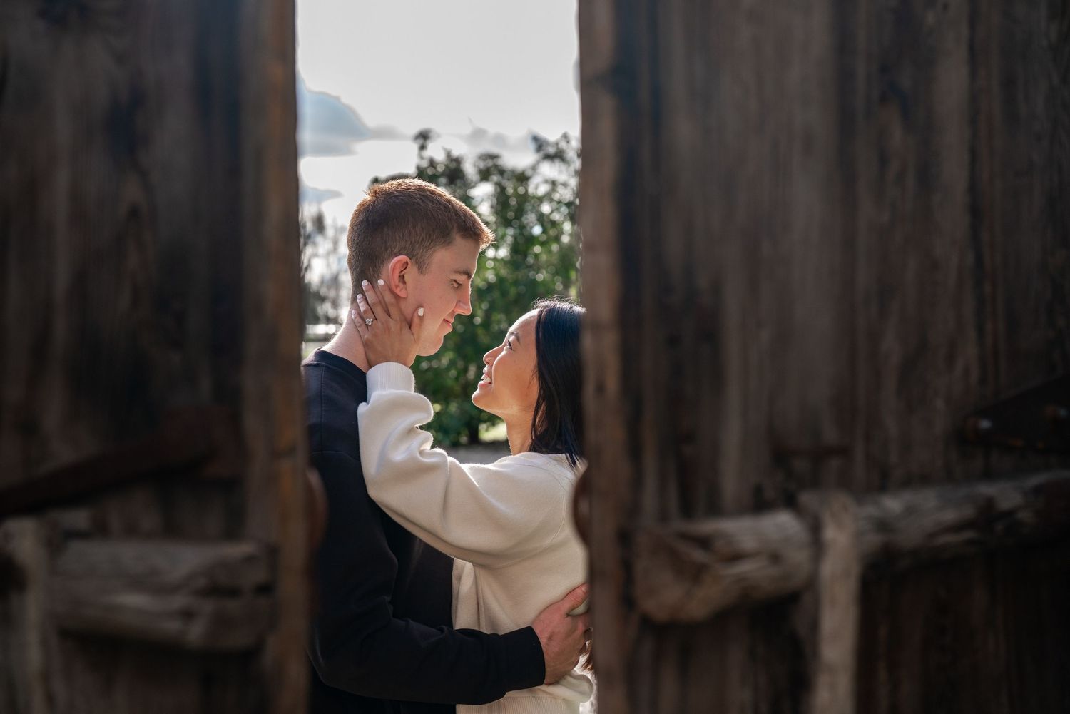 Silhouetted figures share tender moment near wooden structure during golden hour.
