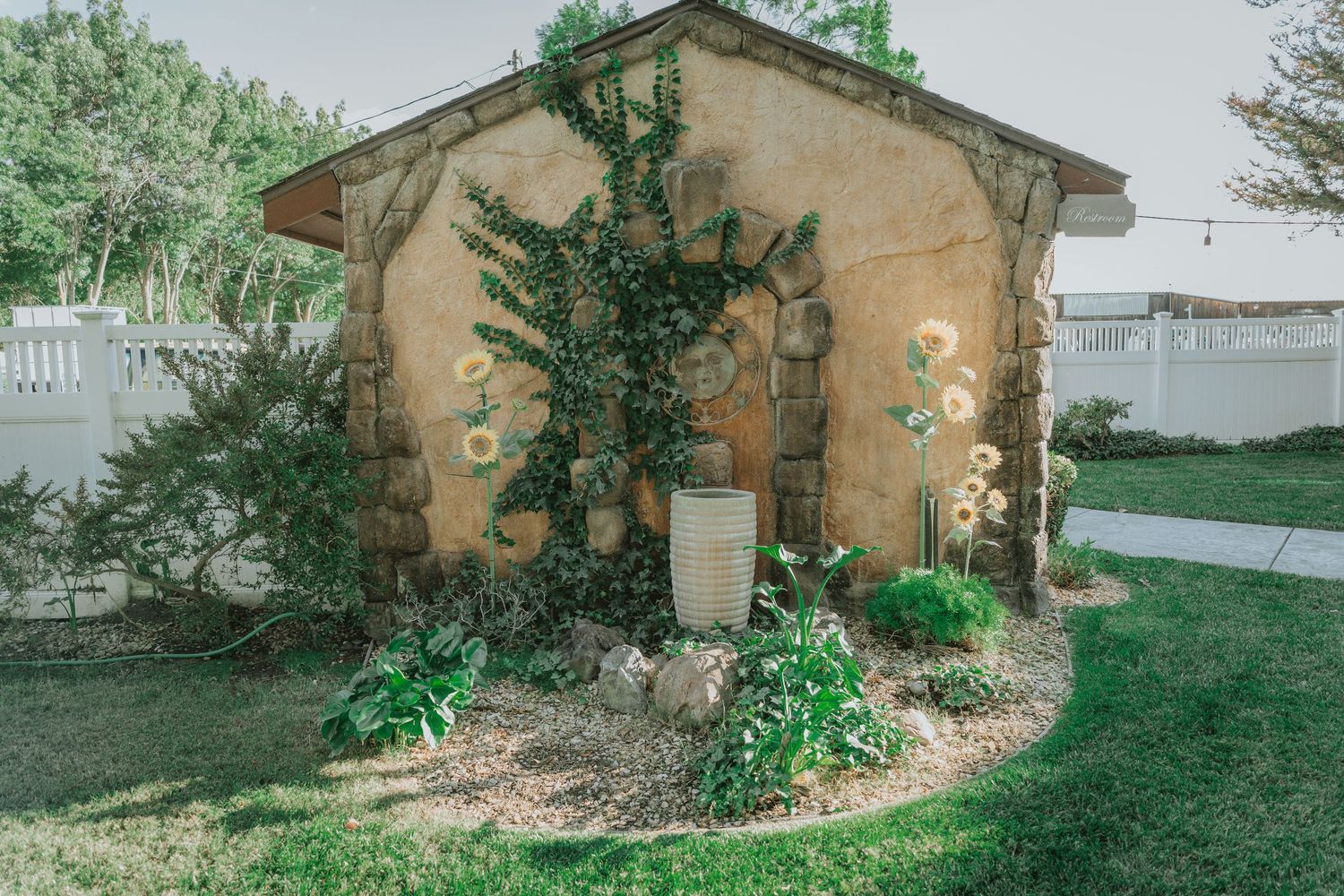 Small garden structure with climbing vines and decorative lighting against a beige wall at La Grande Estates