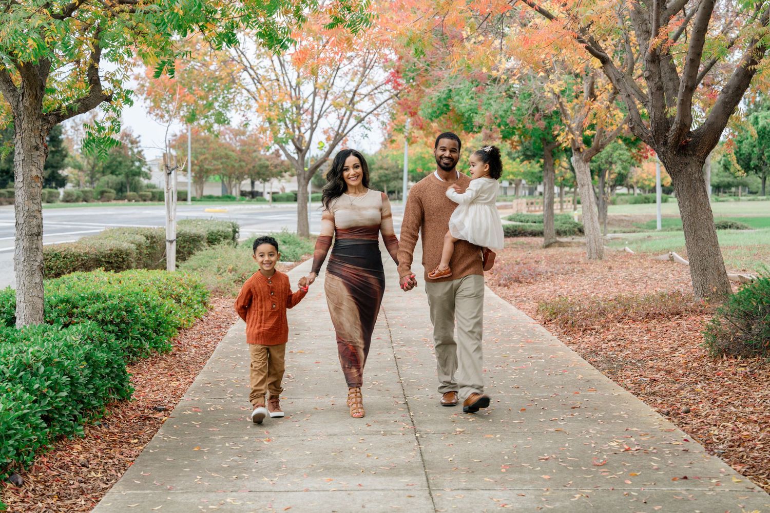 Family walking together on a tree-lined path during fall.