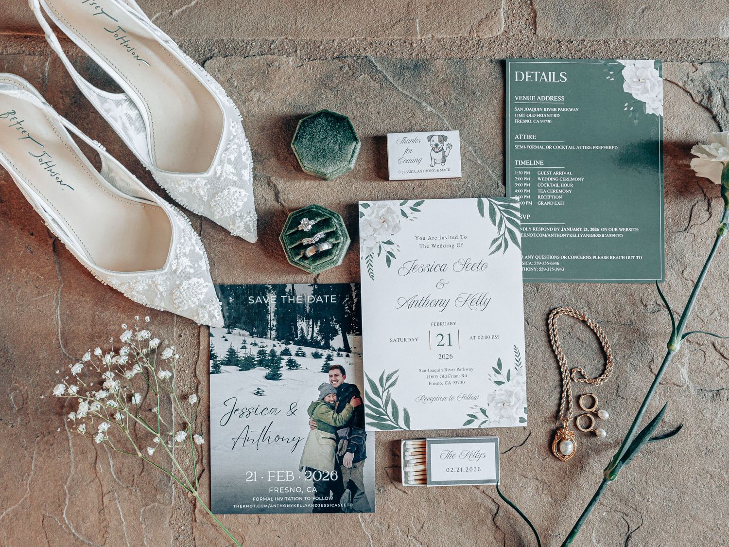 Elegant wedding stationery flat lay featuring green and white invitations, save the dates, lace heels, rings, and floral accents.