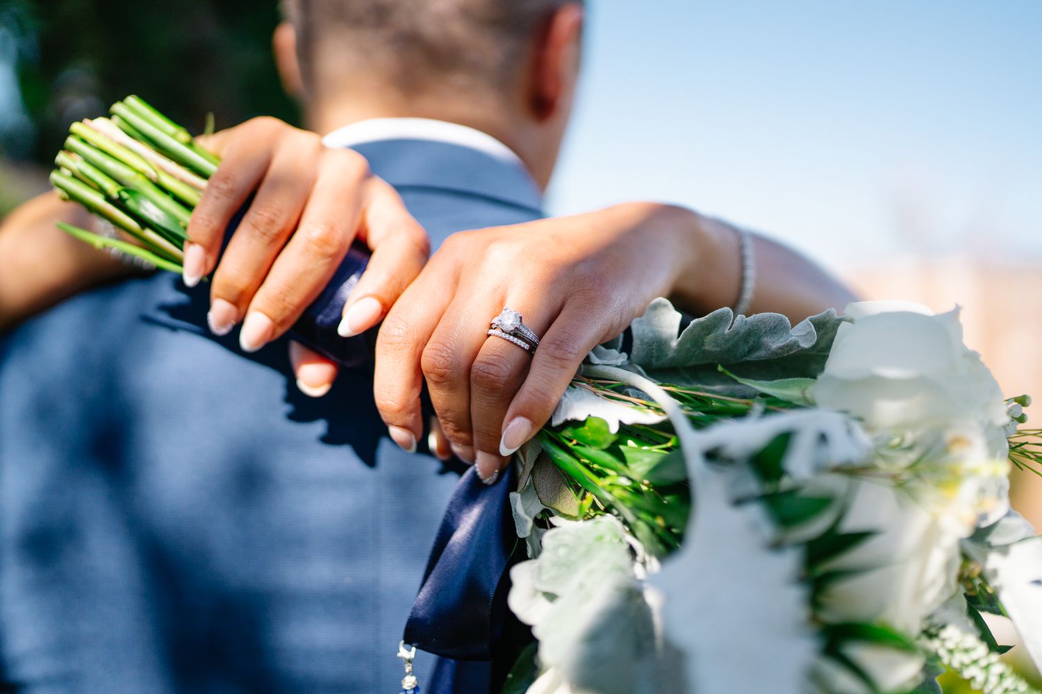 Close-up of hands holding fresh green herbs or flowers against a bright blue sky.