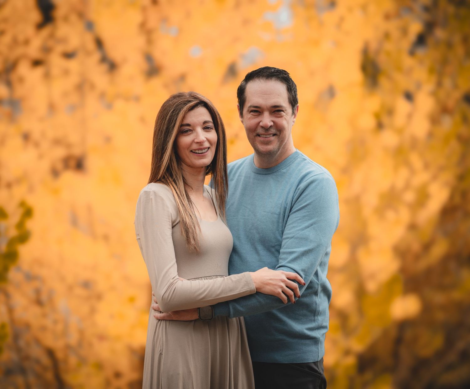 A couple sharing joyful moments against vibrant golden fall foliage.