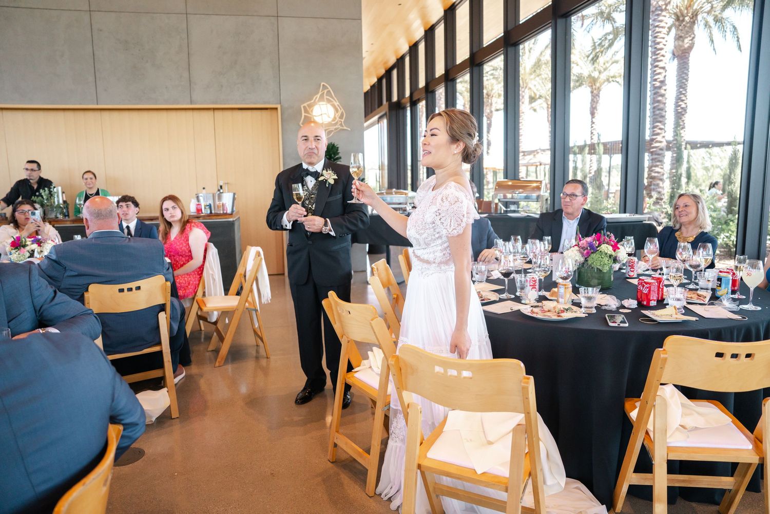 Bride and groom share a toast during their elegant wedding reception with guests seated at black-draped tables.