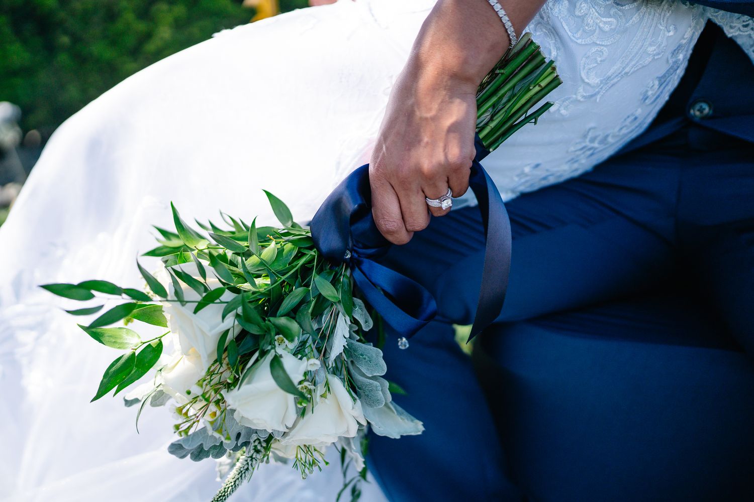 Bride and groom holding a white floral bouquet with navy blue ribbon at a wedding ceremony.