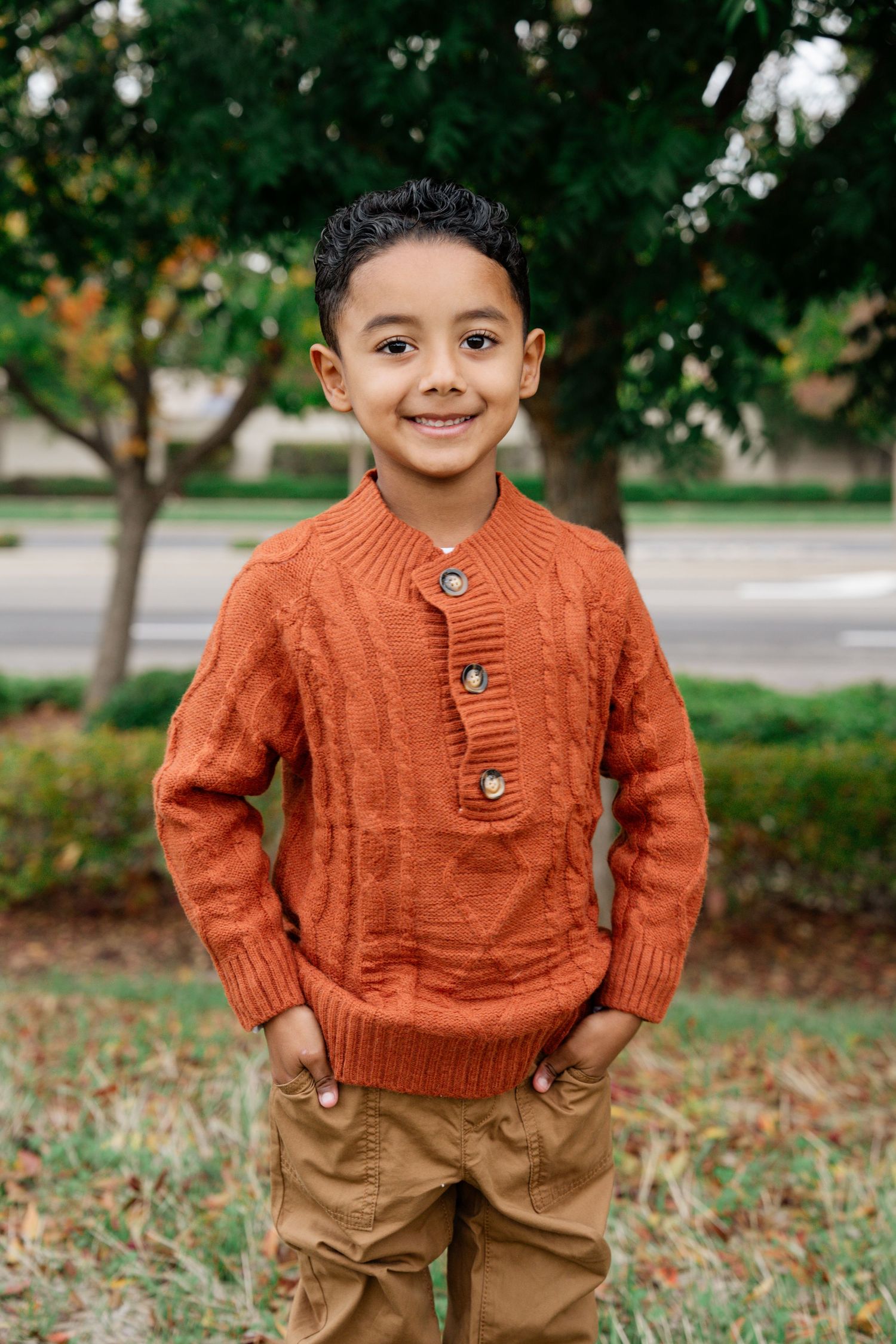 Child wearing an orange sweater poses in a park during fall.