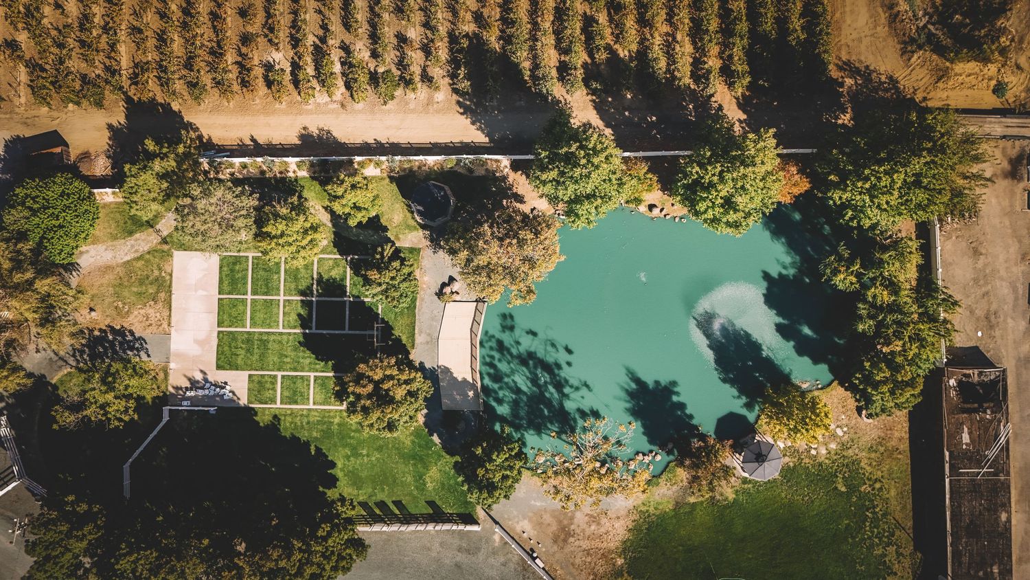 Aerial view of a natural lagoon-style swimming pool surrounded by lush trees and manicured grounds on a rural estate.