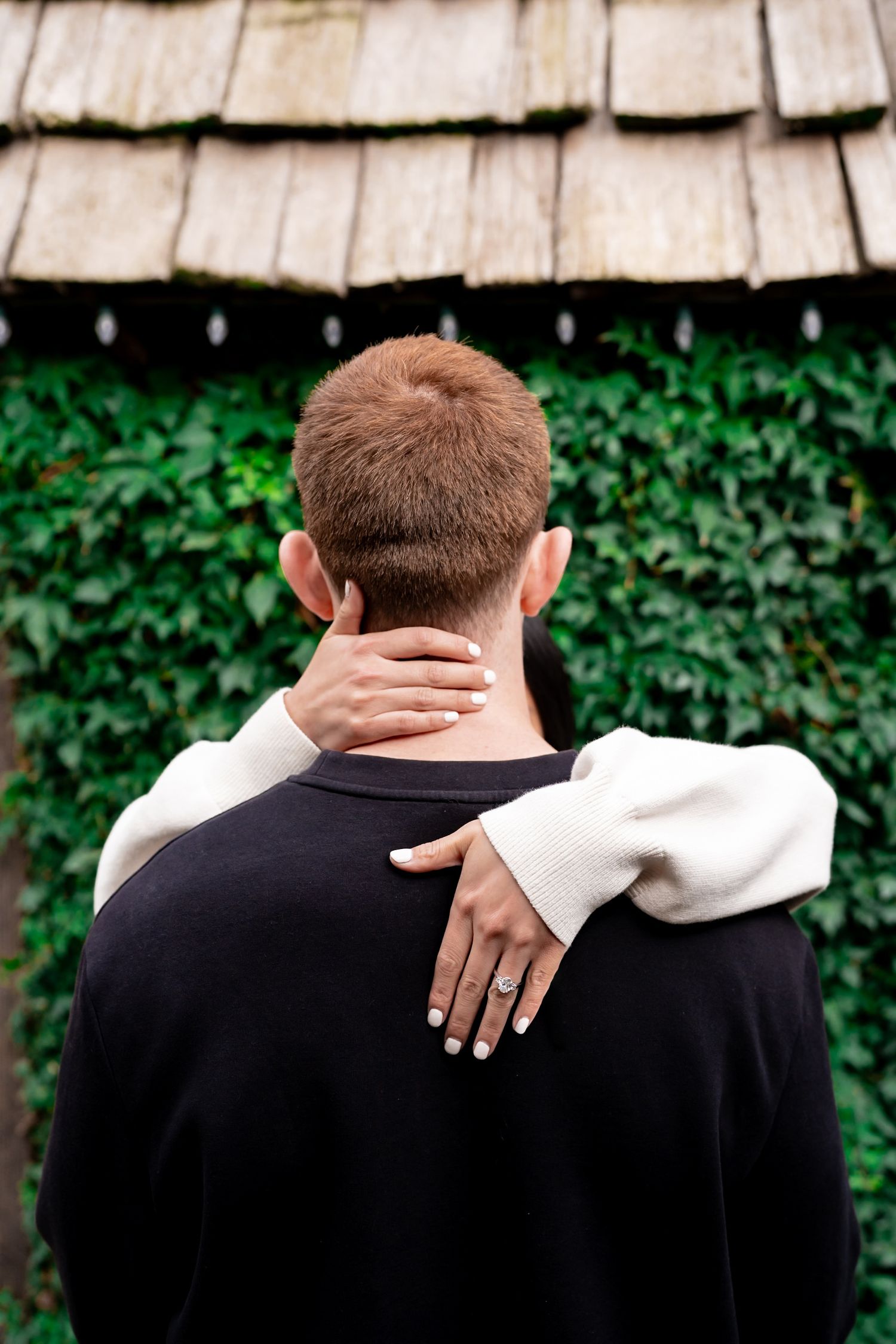 Close-up view of hands embracing from behind against wooden shingle background.