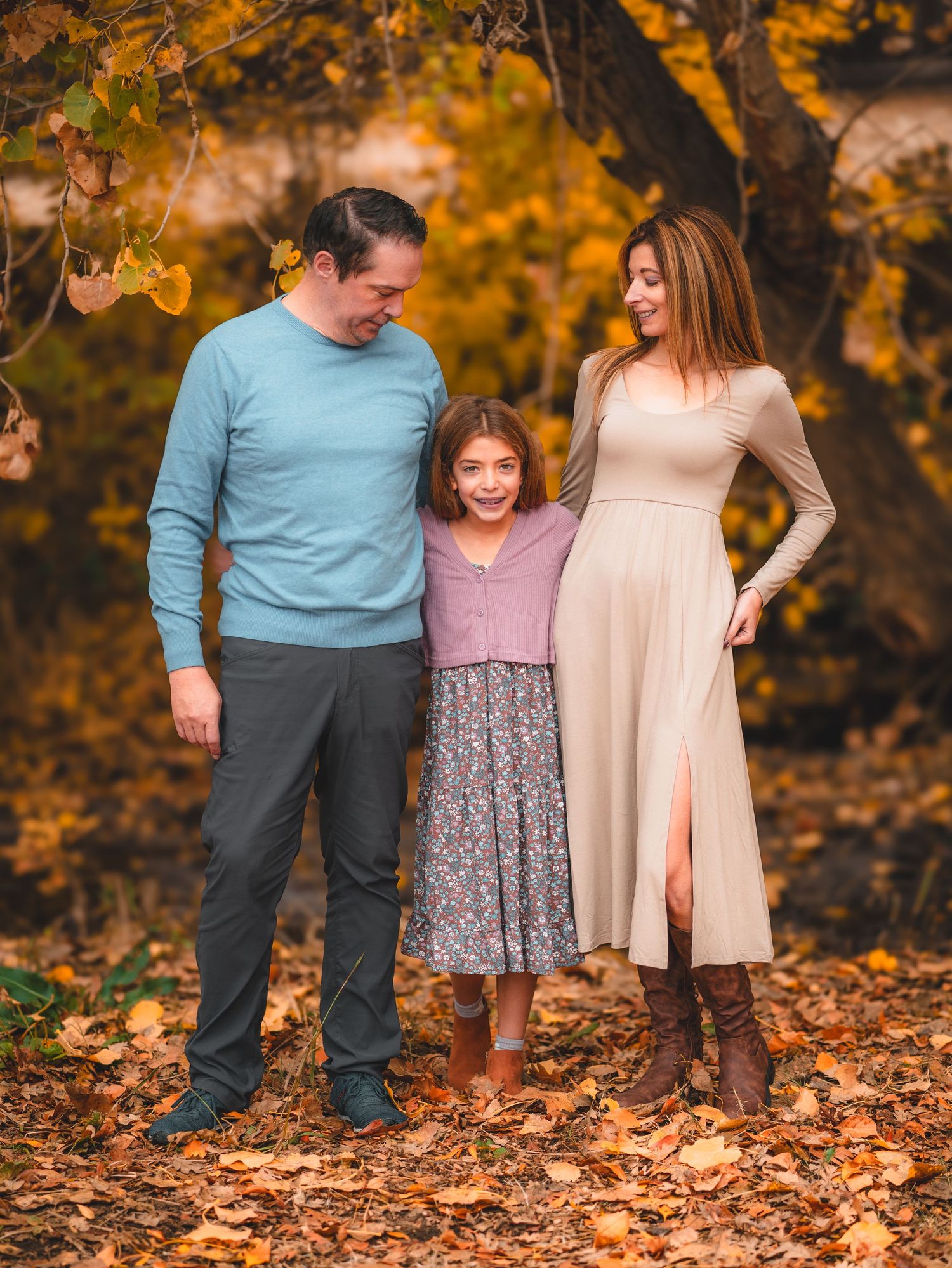Family walking together through colorful autumn leaves in a park during golden hour.