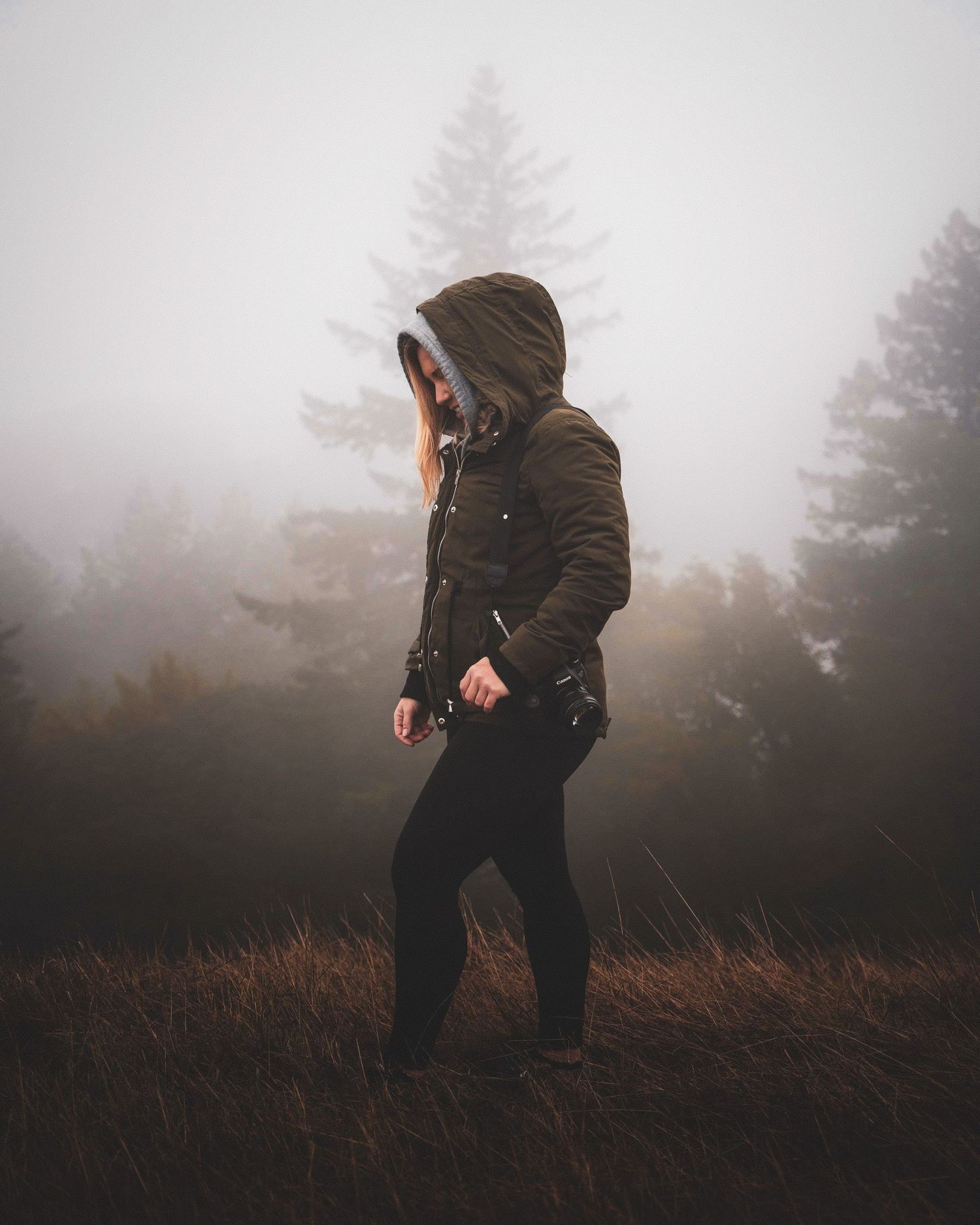 Person in hooded jacket standing in misty forest field on a foggy day.