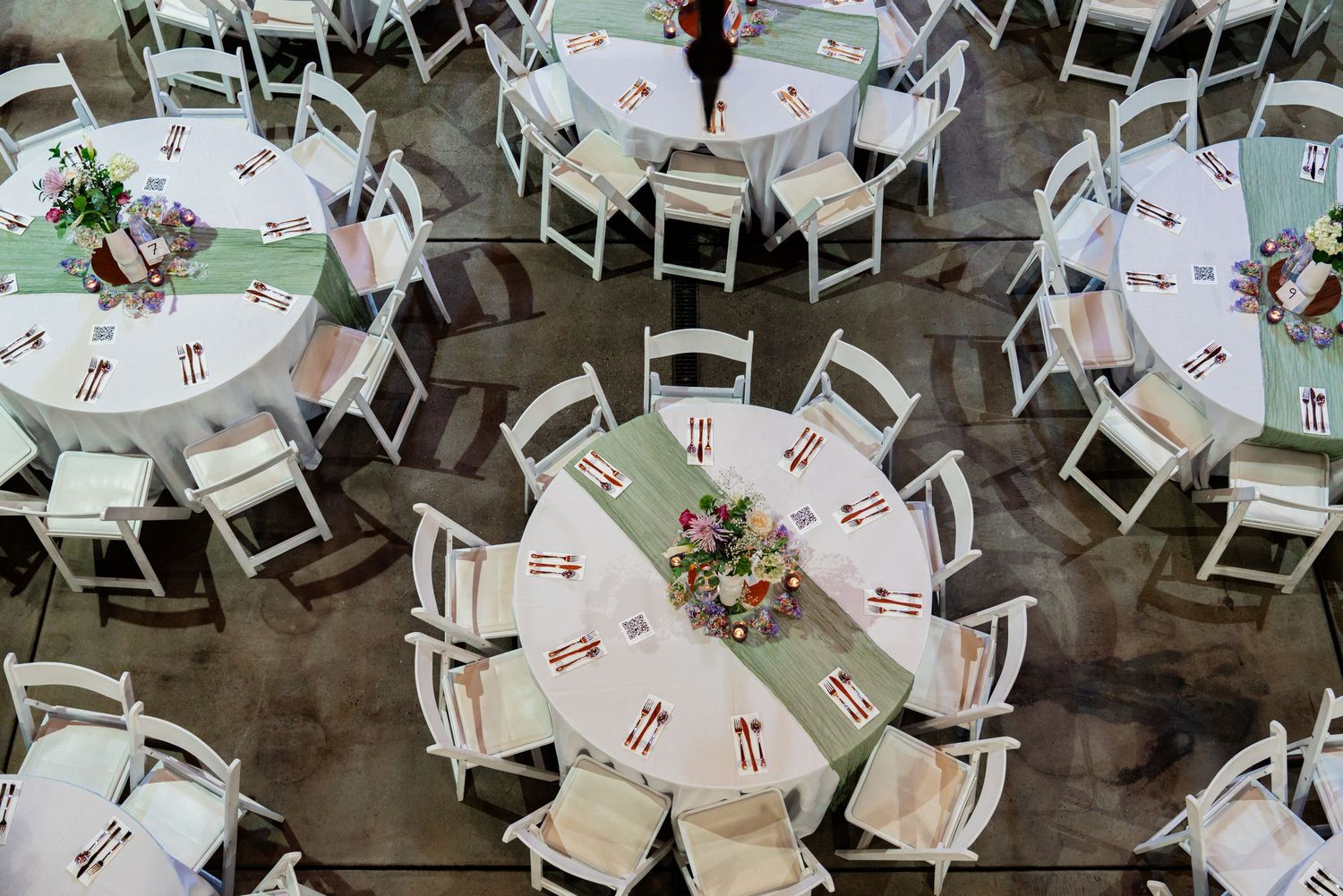Overhead view of wedding reception tables decorated in white and mint green with floral centerpieces.