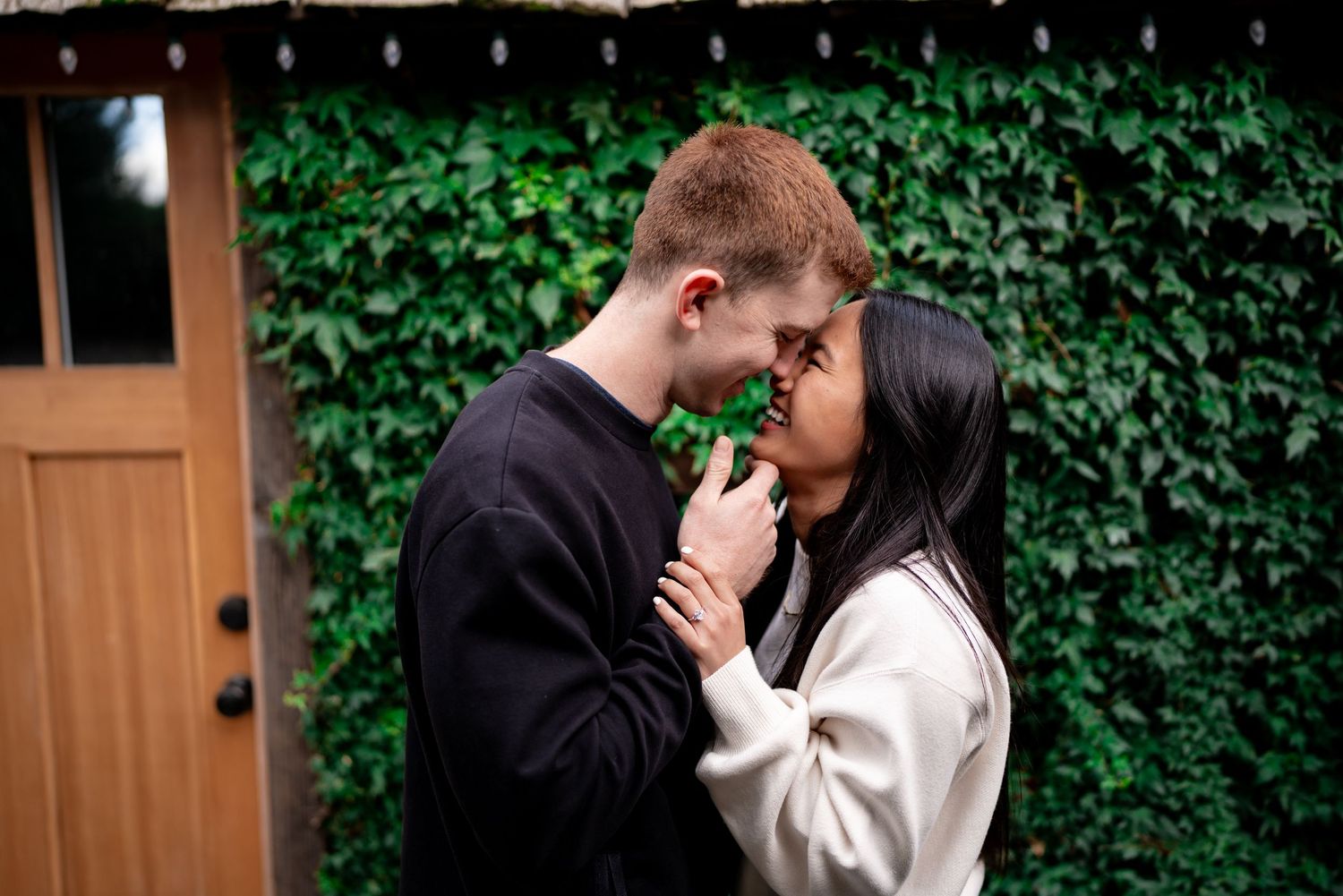 Romantic couple embracing in front of an ivy-covered wall and wooden door.