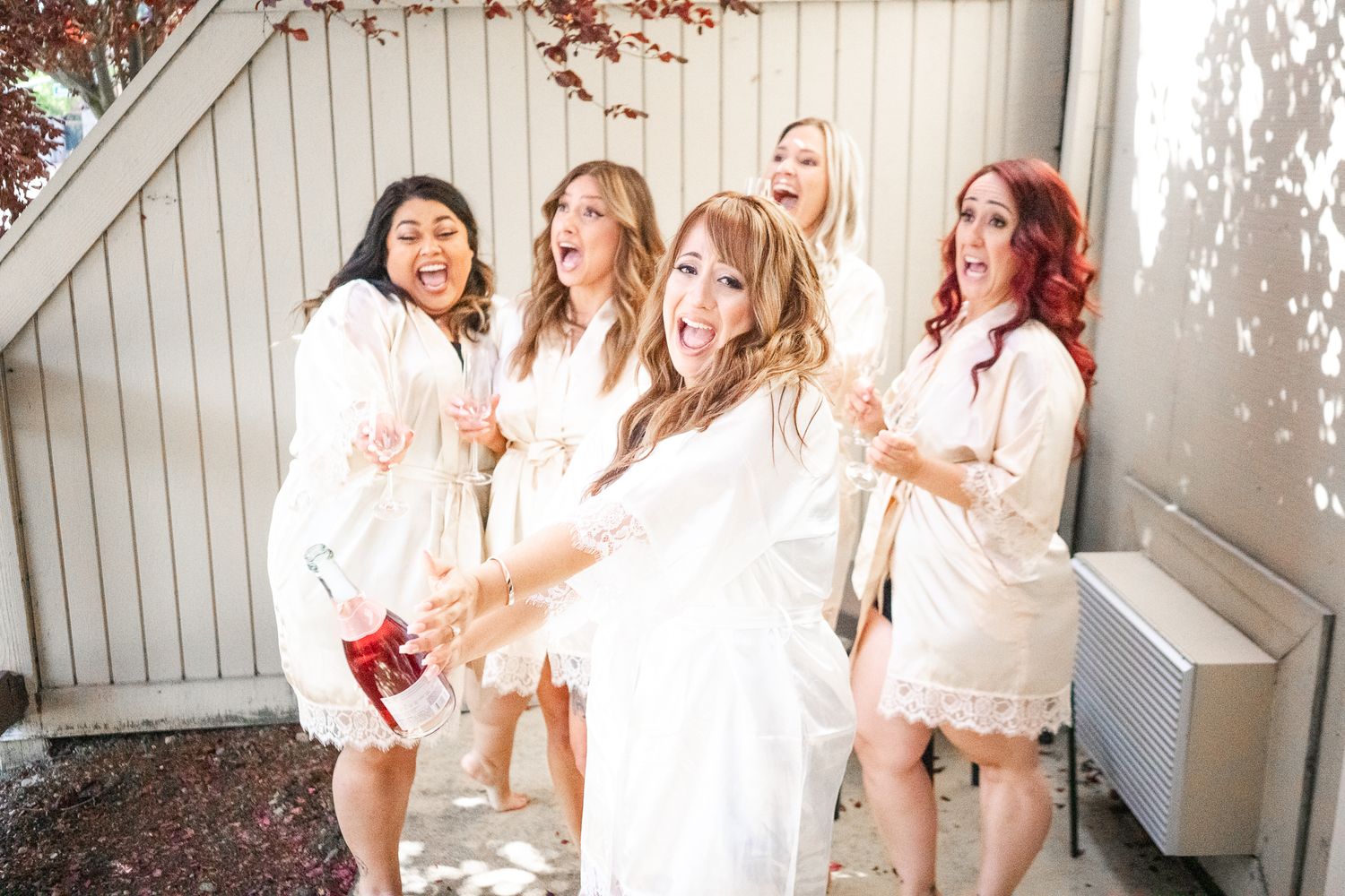 Bride and bridesmaids in white robes laughing and celebrating together before the wedding ceremony.