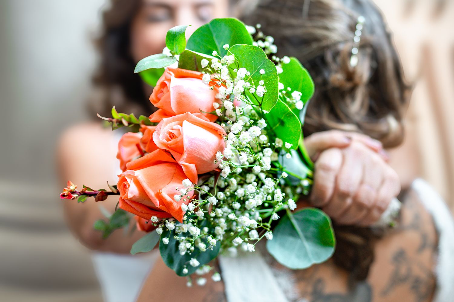 Bride holding a bouquet of orange roses and baby's breath flowers at her wedding.