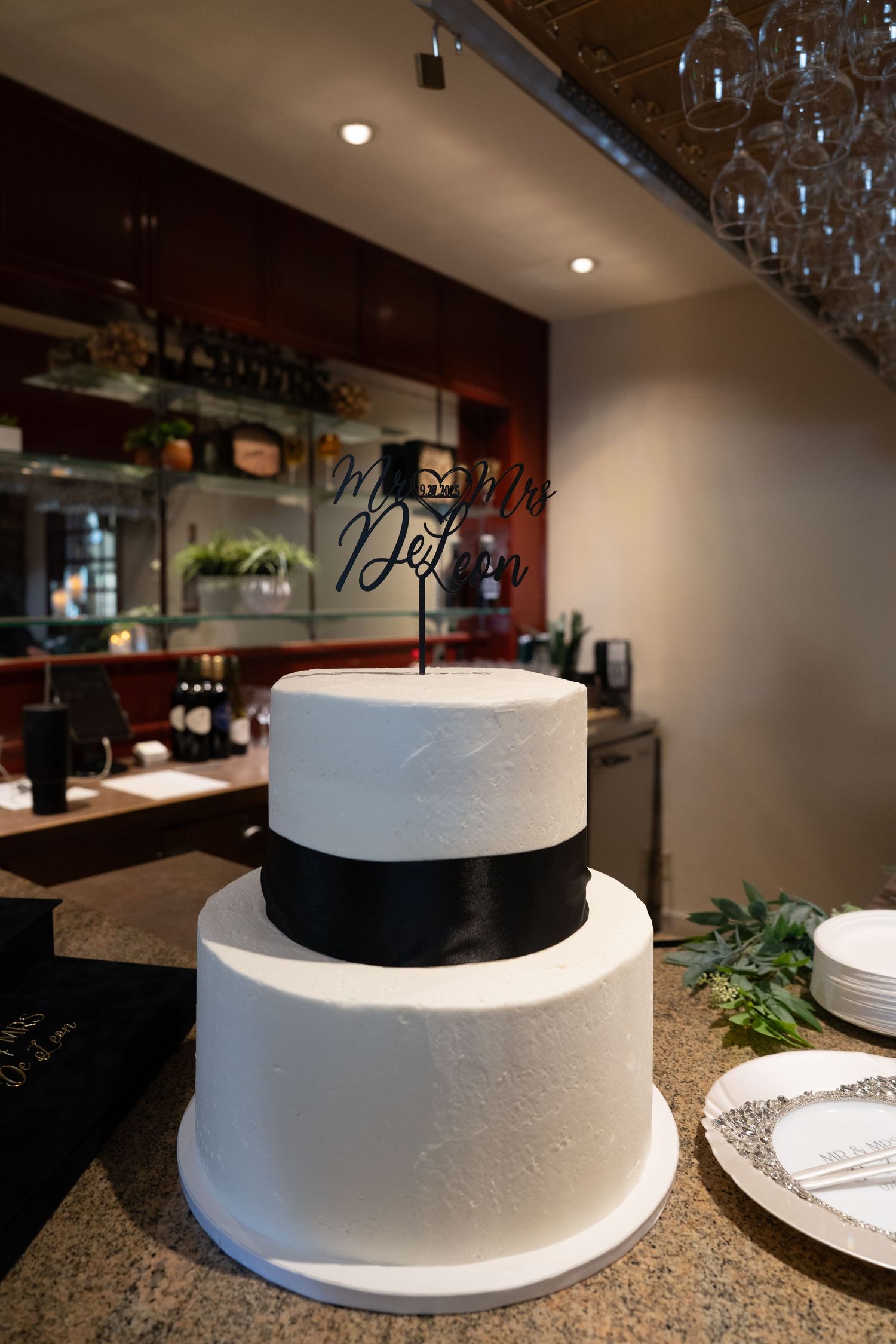 White tiered wedding cake displayed on granite countertop with hanging glassware above at Forest Suits Resorts