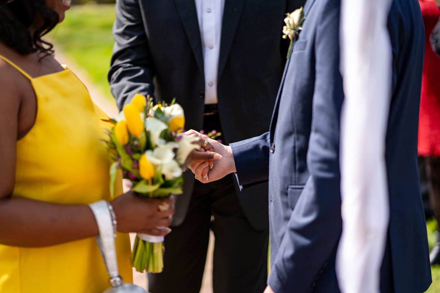 Groom places ring on brides finger during outdoor wedding ceremony, bride holds yellow floral bouquet.