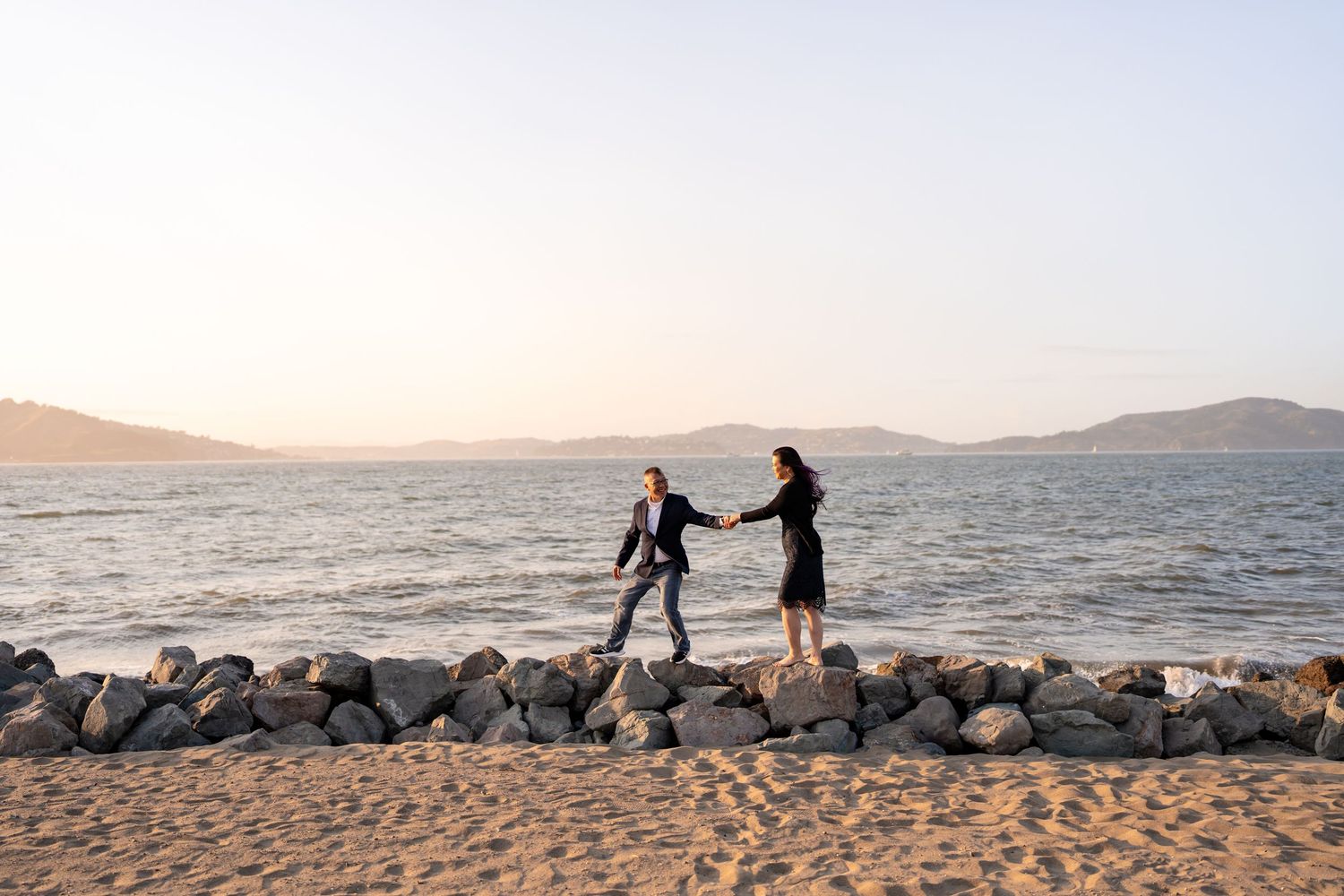 A romantic beach photoshoot with rocky coastline and ocean views at golden hour.