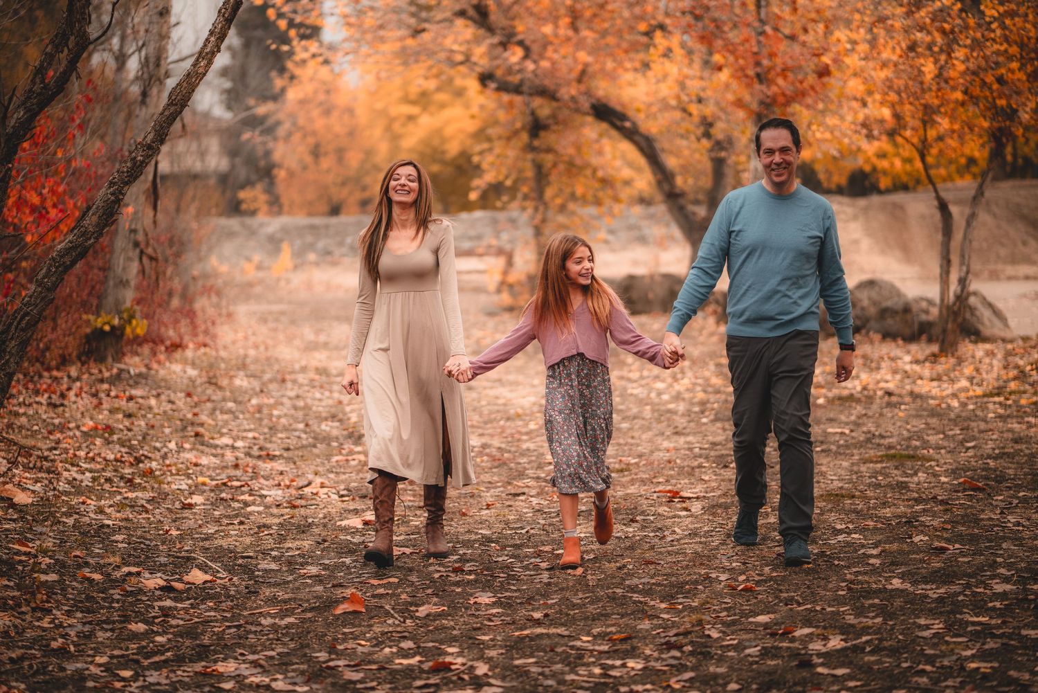 Family walking together through autumn trees with fallen orange leaves.
