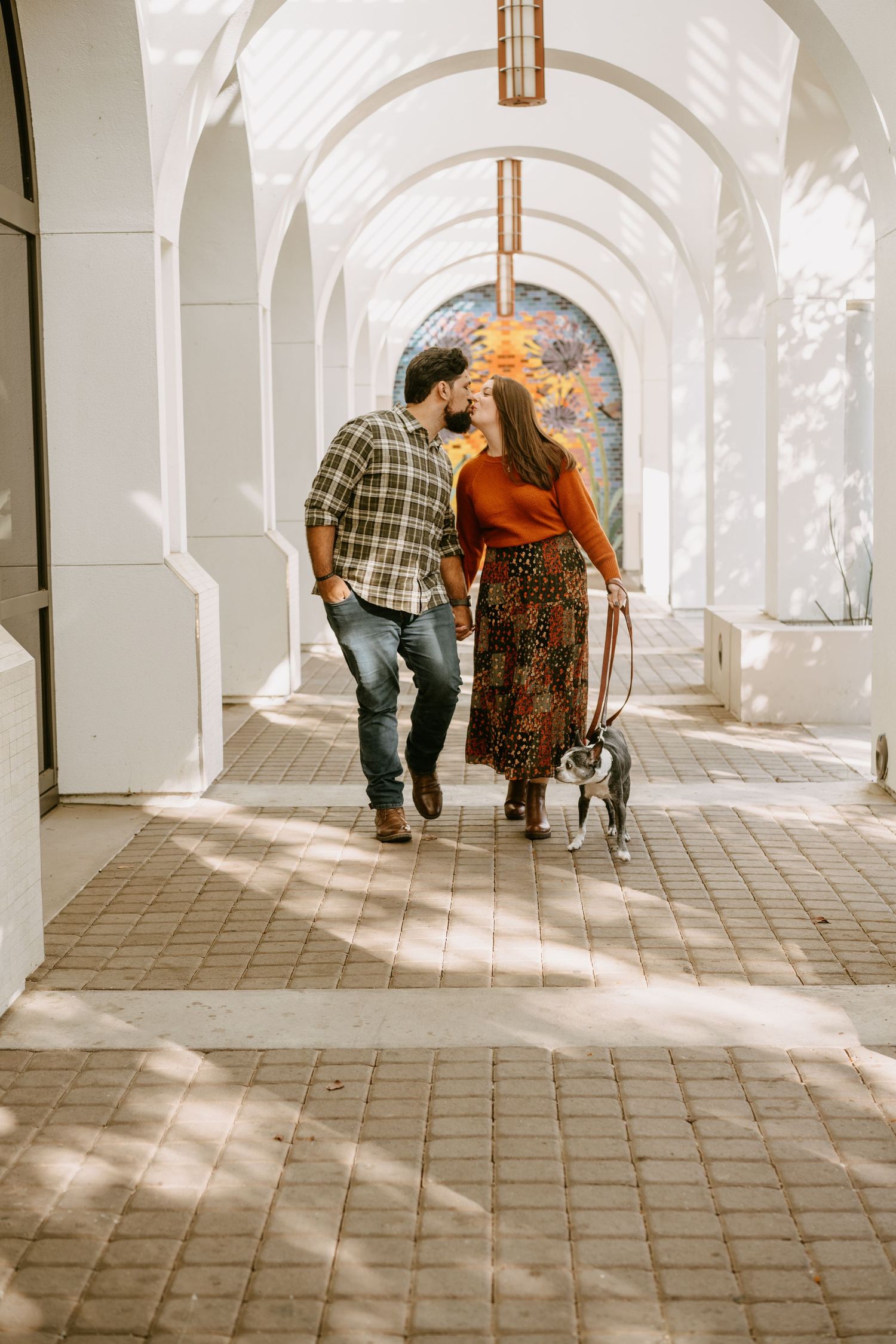 A couple walks through a sunlit archway corridor with beautiful architectural details.