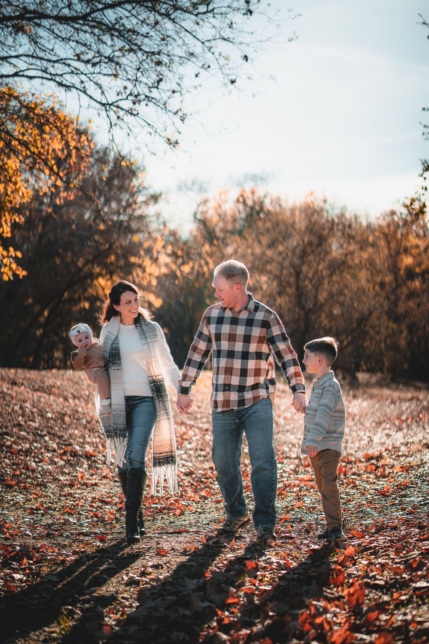 Family walking together through fallen autumn leaves at sunset casting long shadows.