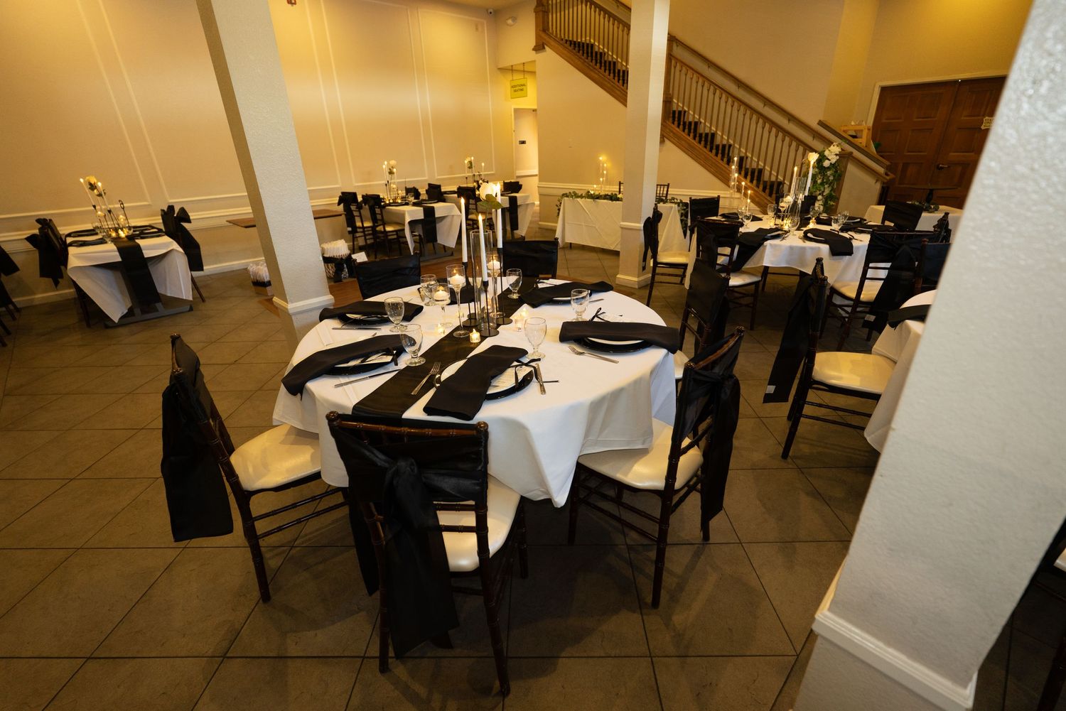 Spacious reception venue with black chairs and white tablecloths set for a formal gathering at Forest Suits Resorts