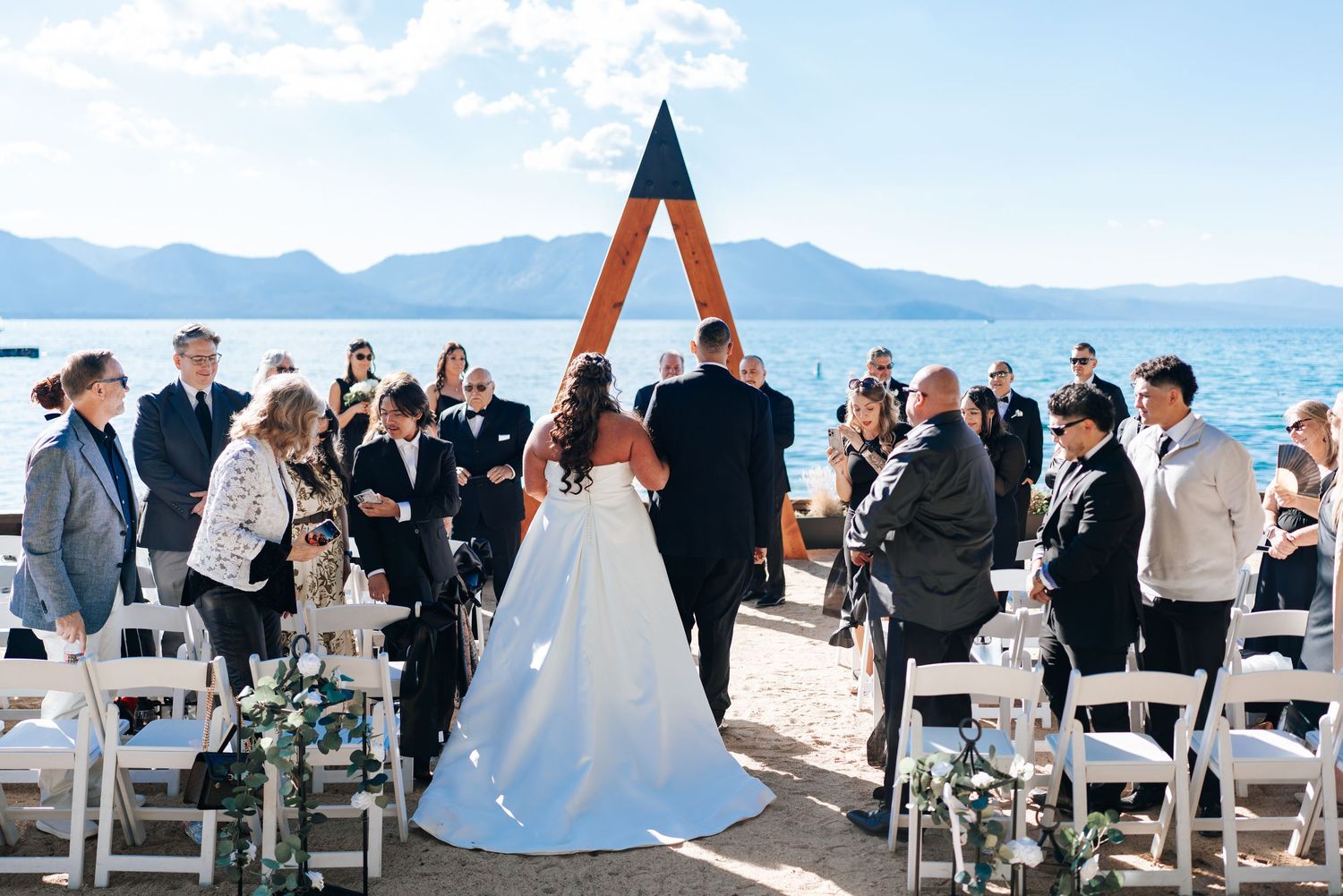Outdoor lakeside wedding ceremony with mountain backdrop and white chairs.