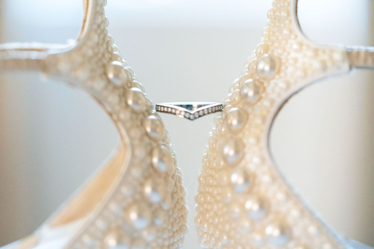 Pearl-embellished wedding heels framing a delicate diamond chevron ring on a soft white background.