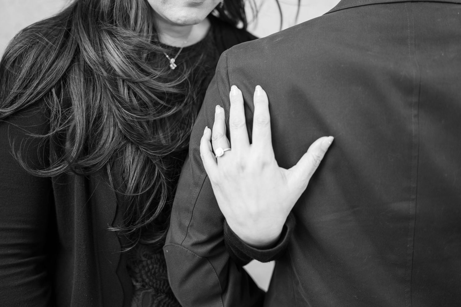 Black and white photo of a couple embracing, woman's hand with engagement ring resting on man's back.