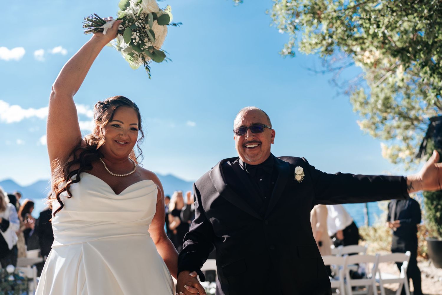 Joyful newlyweds celebrate after outdoor wedding ceremony with mountain backdrop and blue sky.