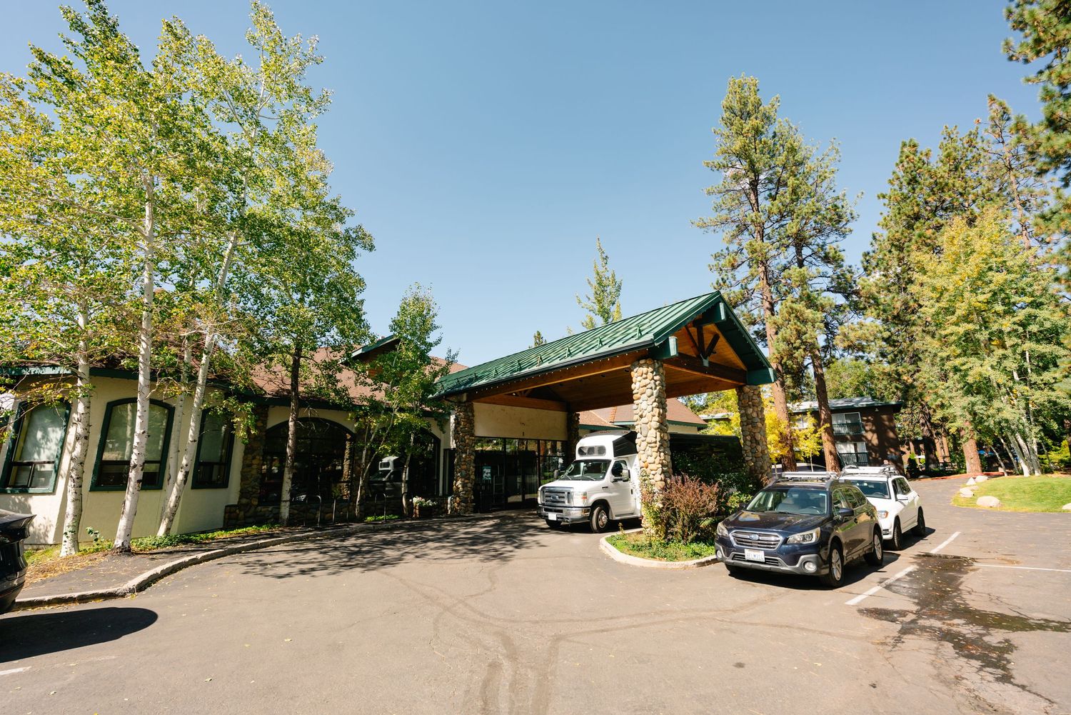Panoramic view of venue exterior with parked cars and green trees on sunny day at Forest Suits Resorts