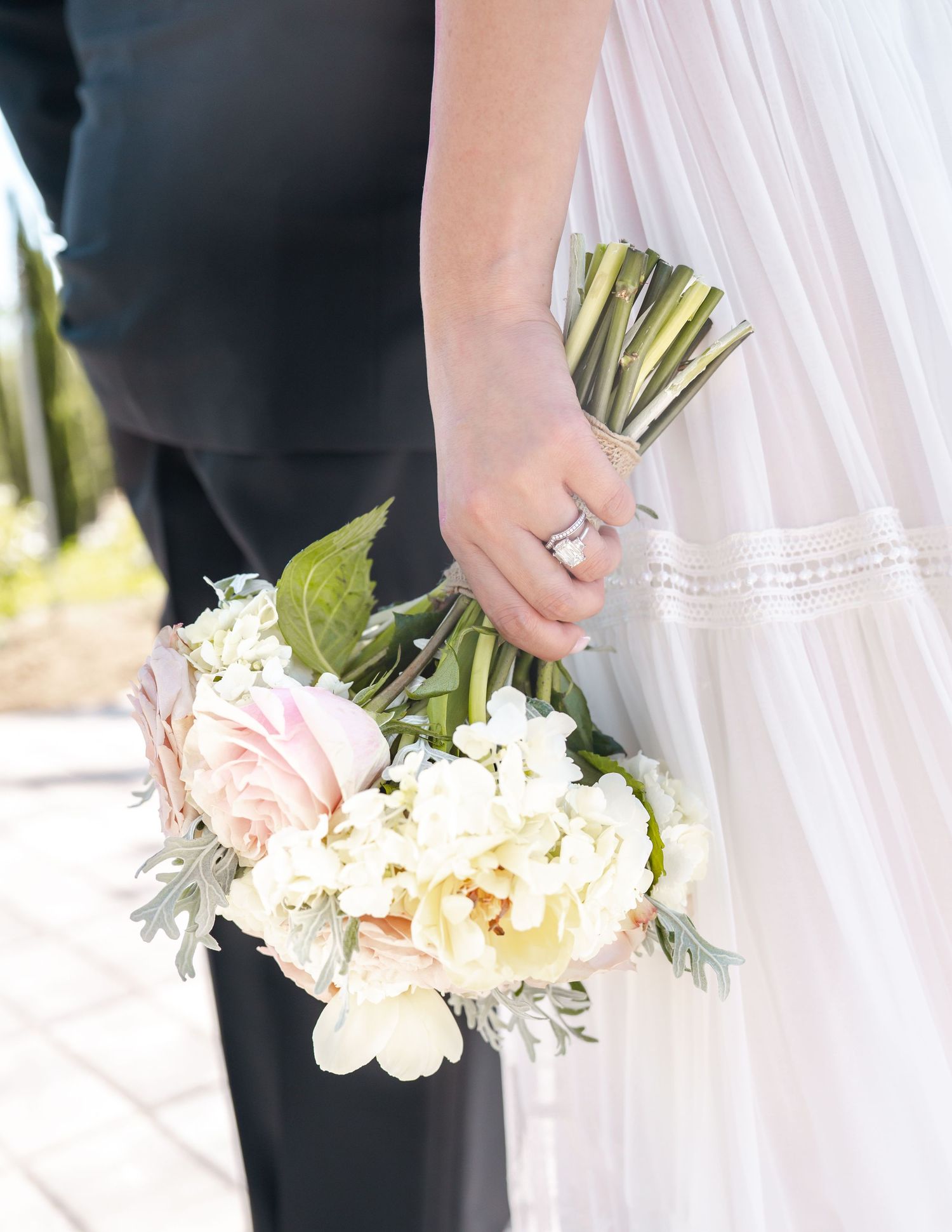 Bride holding a delicate wedding bouquet of blush roses and white peonies, wearing a diamond ring in a white gown.
