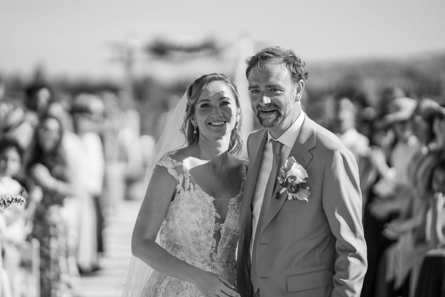 Black and white photo of a smiling bride and groom at outdoor wedding ceremony.