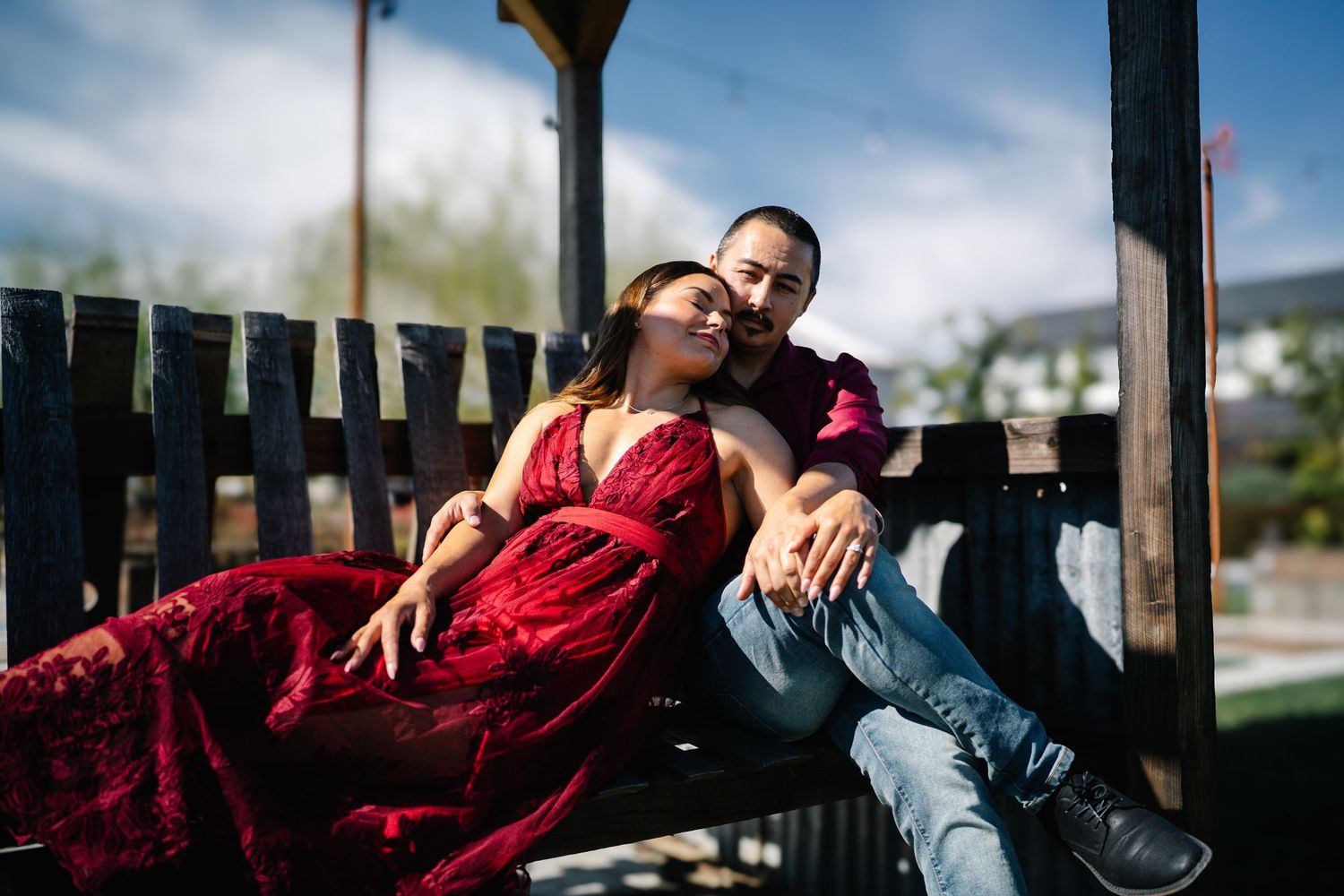 Couple in red dress and jeans relaxing on wooden bench swing under gazebo in outdoor setting at Serendipity Cellars Winery