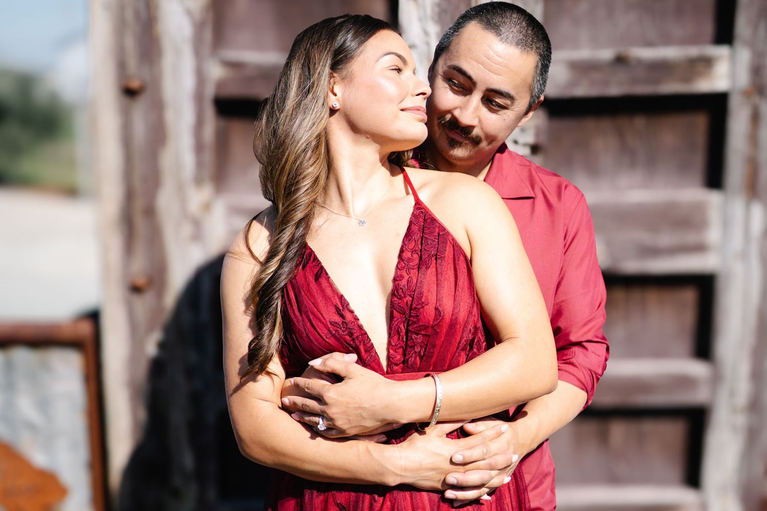 Couple in matching red outfits embracing romantically near rustic wooden doors outdoors at Serendipity Cellars Winery