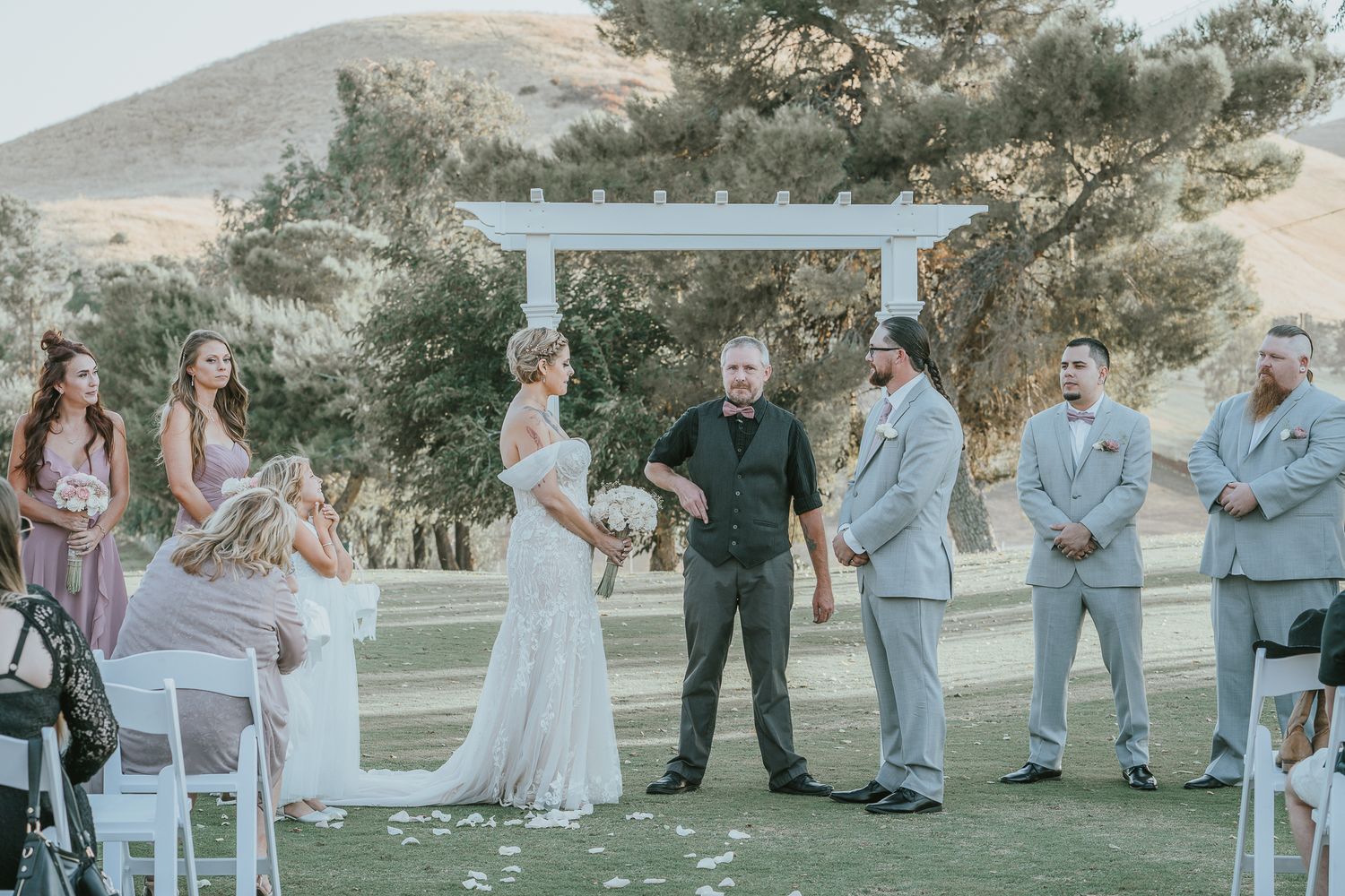 Bride and groom share vows at an outdoor wedding ceremony with bridal party on a golf course.