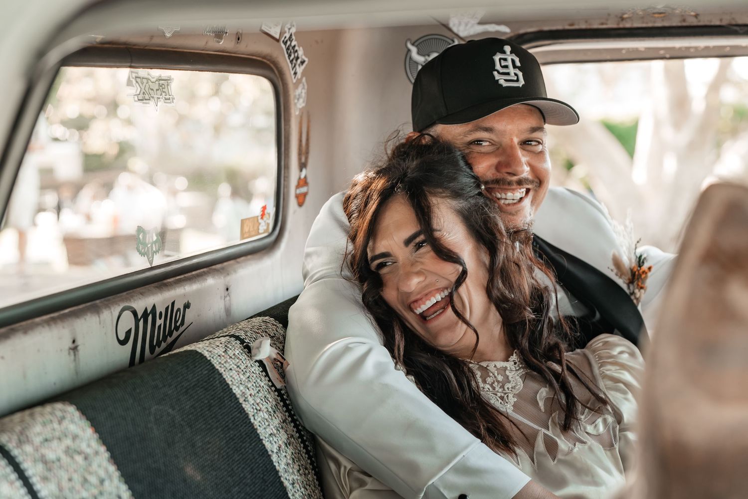 Happy couple embracing and smiling inside a vintage truck, woman with long dark hair, man wearing a baseball cap.