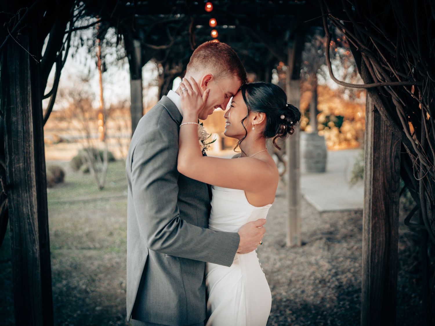 A couple shares a romantic kiss under a rustic wooden arch at their outdoor wedding ceremony at dusk.