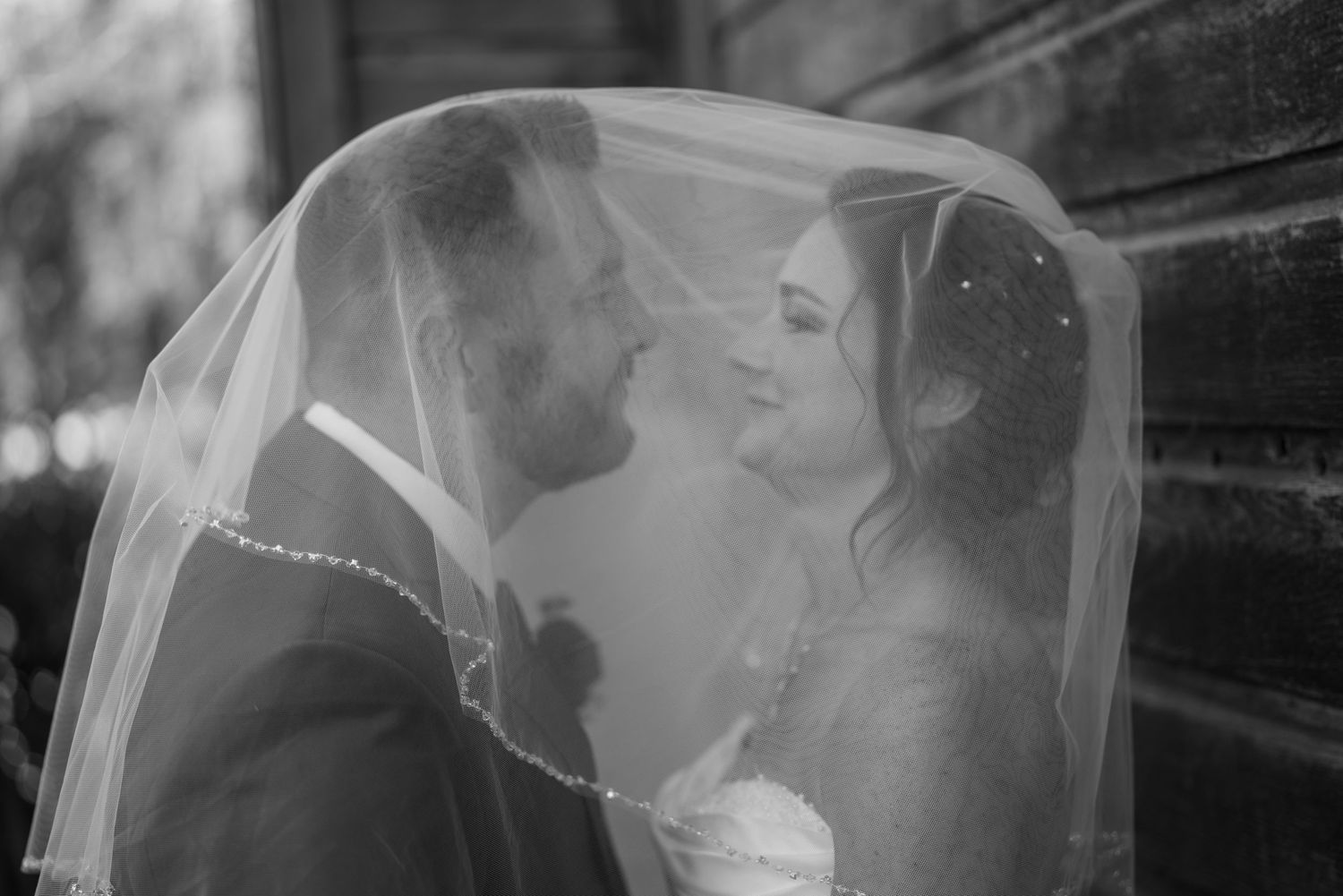 Black and white photo of bride and groom sharing intimate moment under wedding veil.