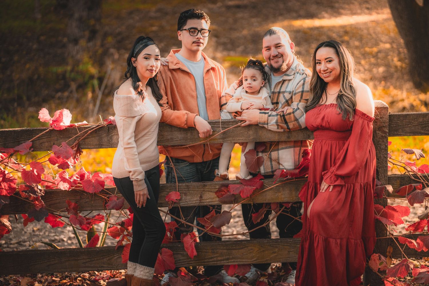 Family enjoying a playful moment together on a rustic wooden bench with red autumn leaves.