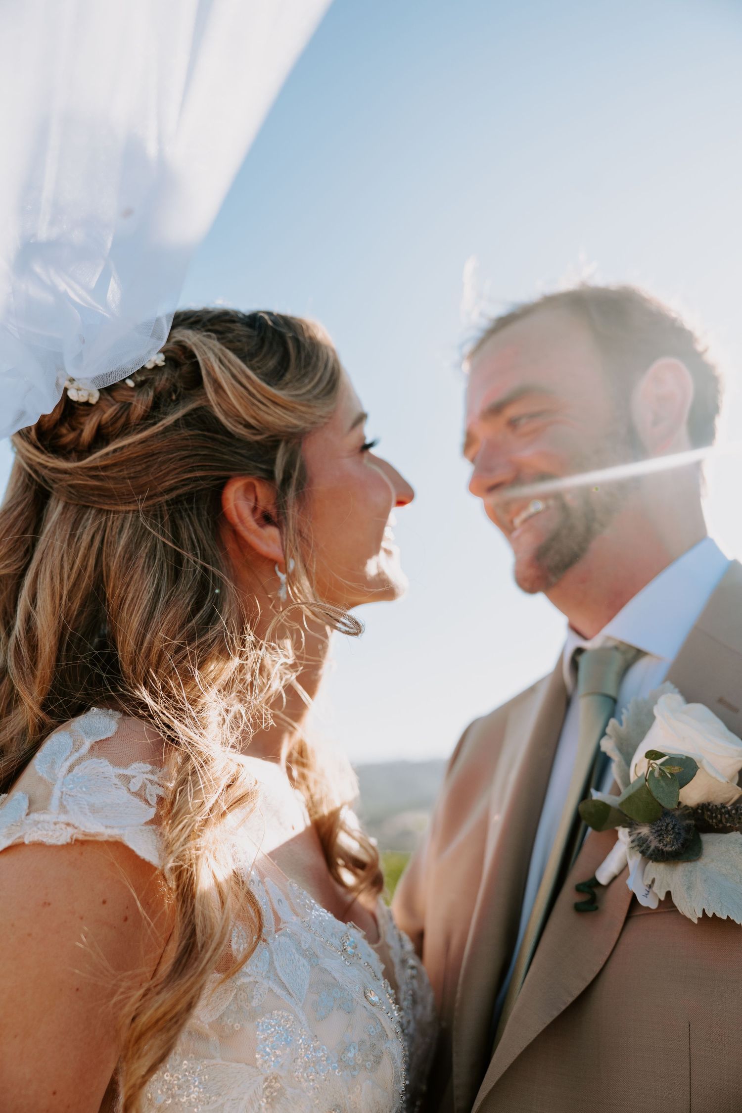 Candid wedding portrait with sunlit couple sharing joyful moment.