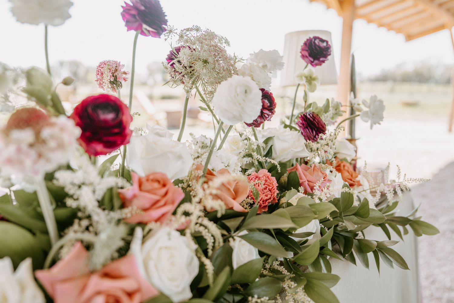 Elegant wedding floral arrangement featuring pink roses, burgundy ranunculus, and white blooms with lush greenery.